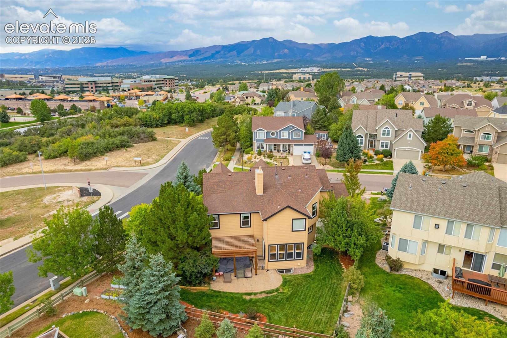 Expansive mountain backdrop, residential neighborhood setting, mature landscaping, multi-level dwelling, and a rear patio