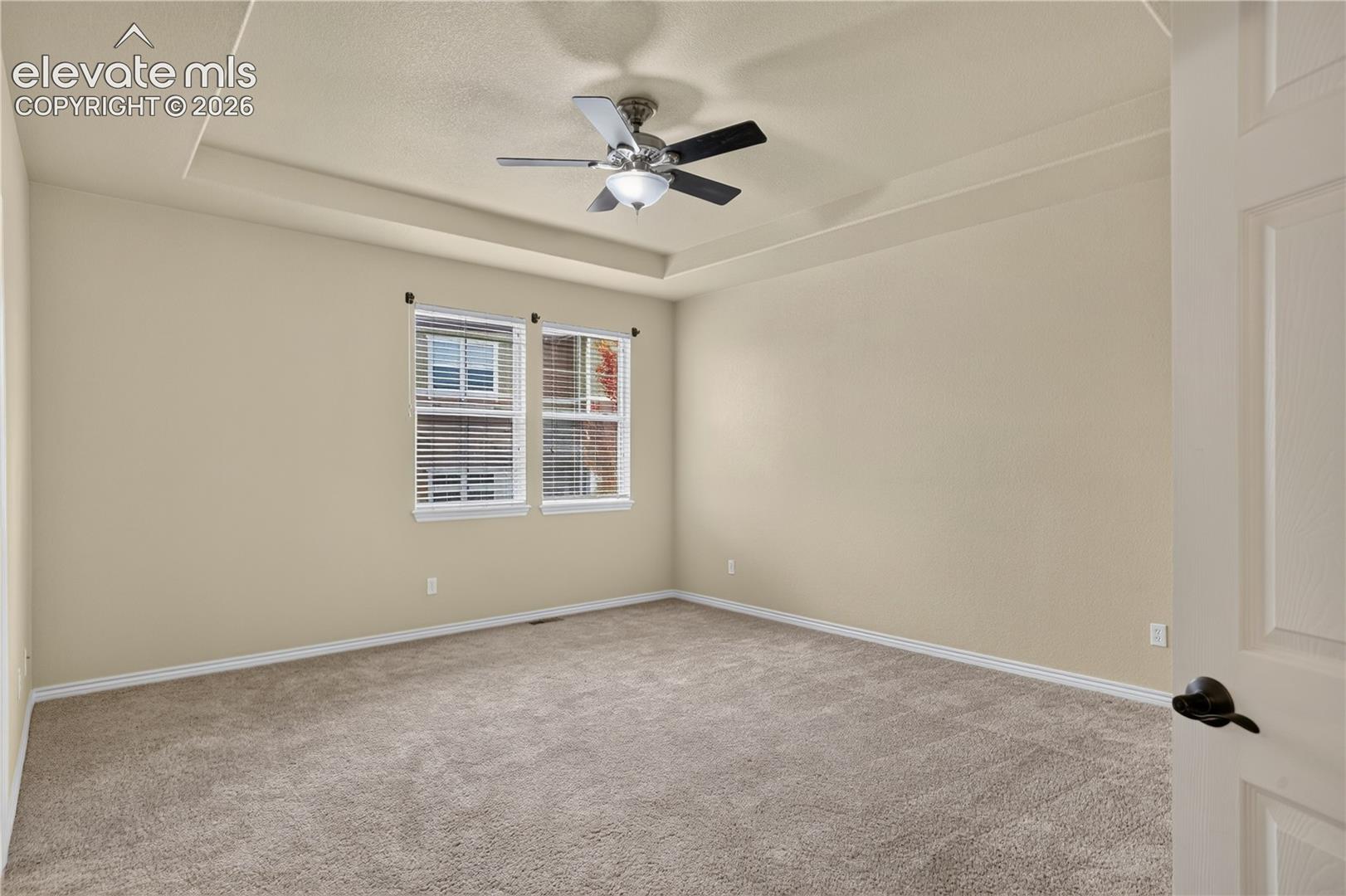 Primary bedroom featuring a tray ceiling, wall-to-wall carpeting, and a central ceiling fan with an integrated light fixture