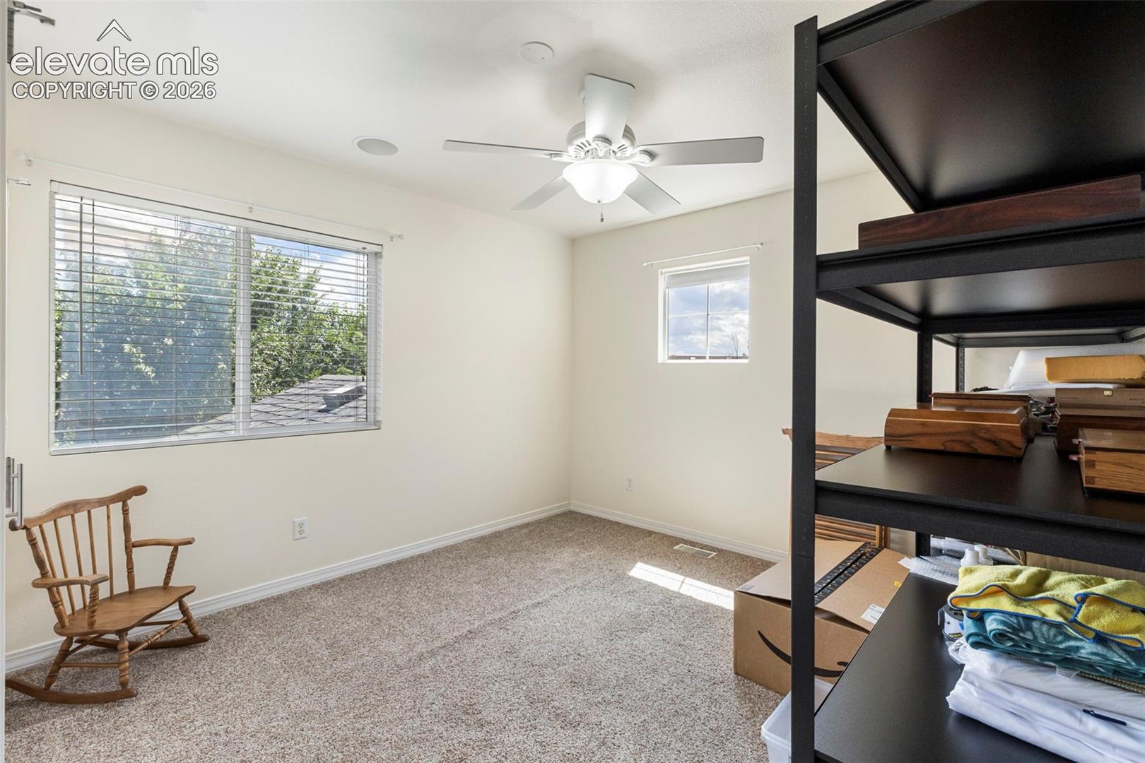 Recessed ceiling speaker, overhead ceiling fan with light fixture, large window with blinds, additional window, and neutral wall color