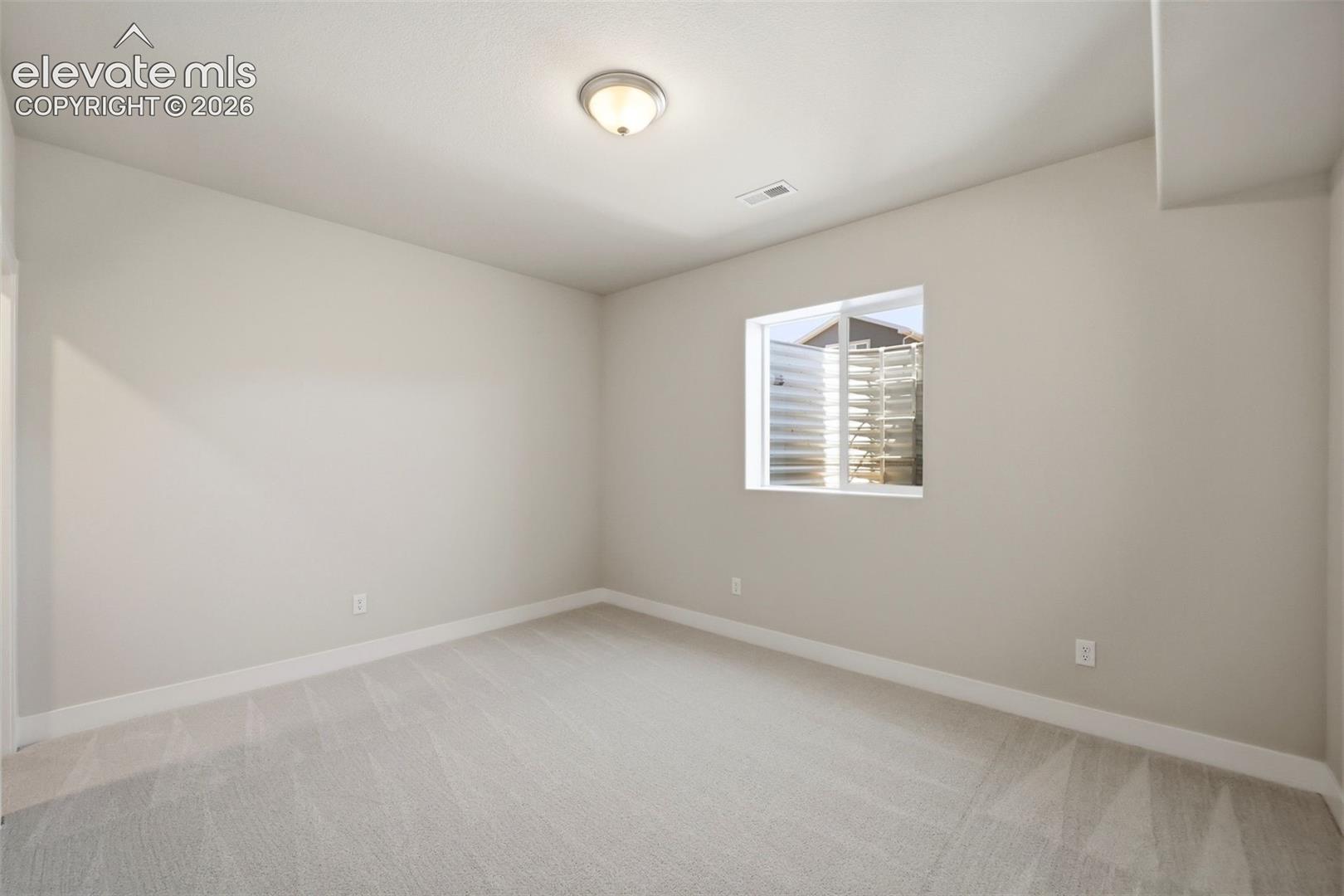 Neutral-toned interior room featuring wall-to-wall carpeting, a single window with a window well, and a flush-mount overhead light fixture