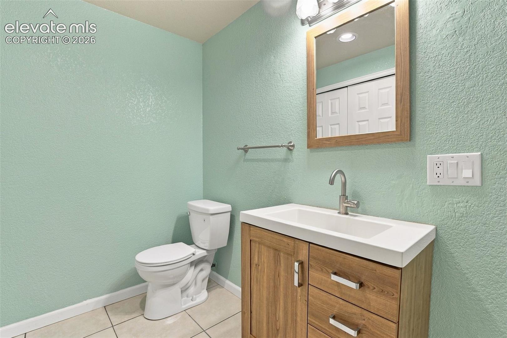 Lower level bathroom featuring a wood-finish vanity with a rectangular sink, brushed-nickel faucet, framed wall mirror, and neutral tile flooring