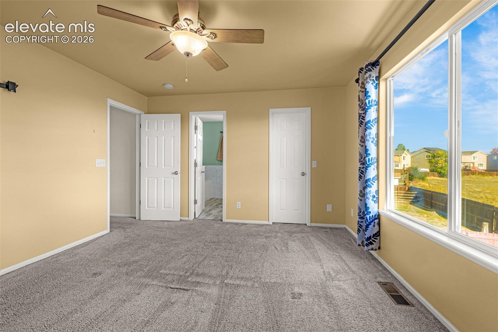Room featuring neutral wall tones, wall-to-wall carpeting, a multi-blade ceiling fan with integrated lighting, and a large window with exterior exposure