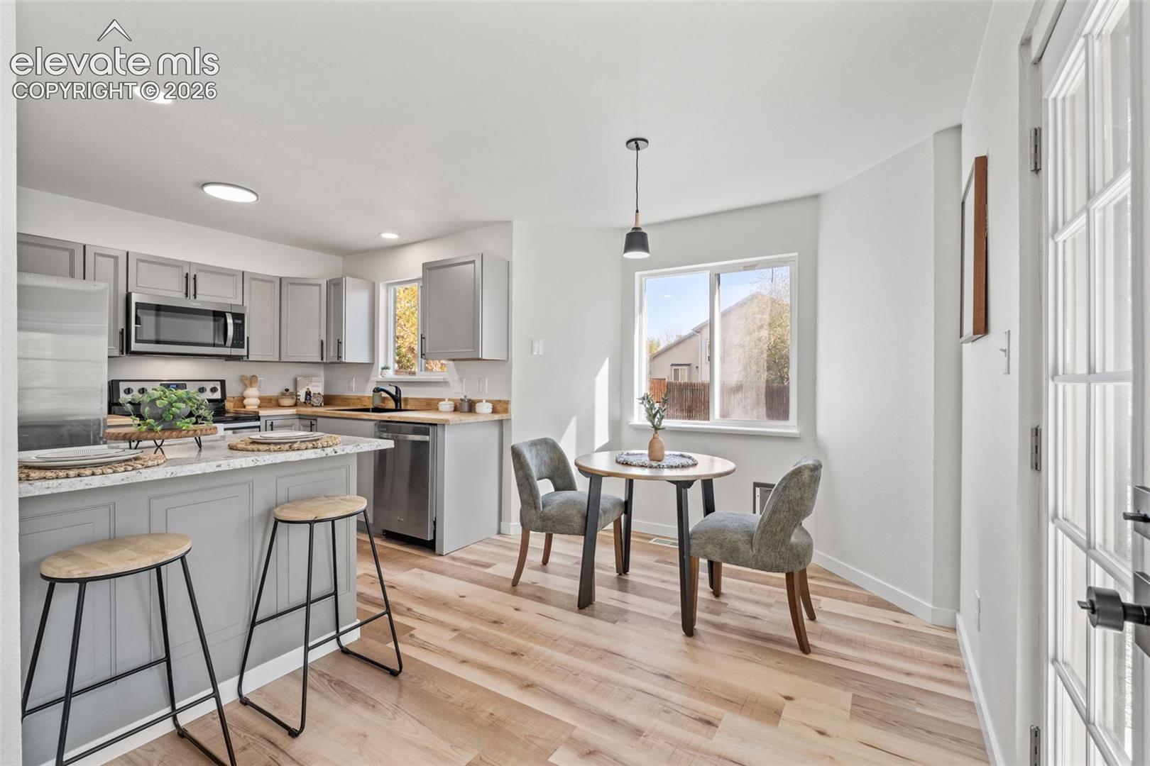 Kitchen featuring shaker-style cabinetry, stone-surface countertops, stainless steel appliances, wood-finish flooring, and a glass-paned door