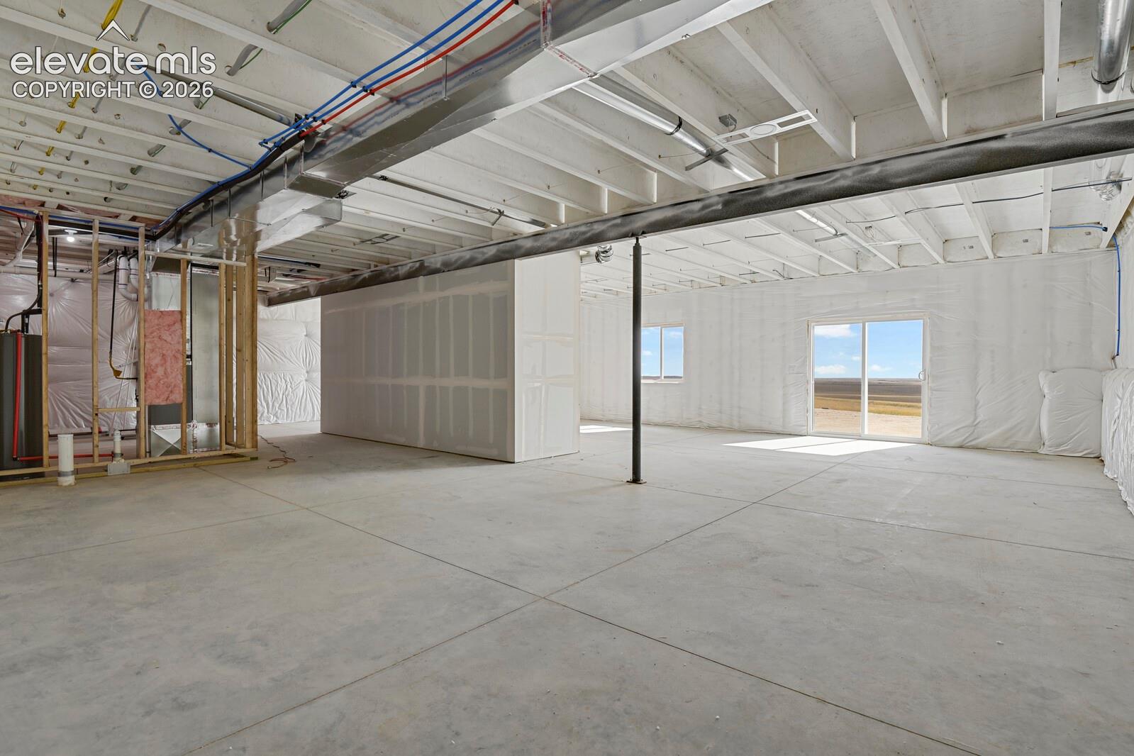 Unfinished interior space featuring concrete flooring, exposed ceiling joists, white vapor barrier insulation, and sliding glass doors