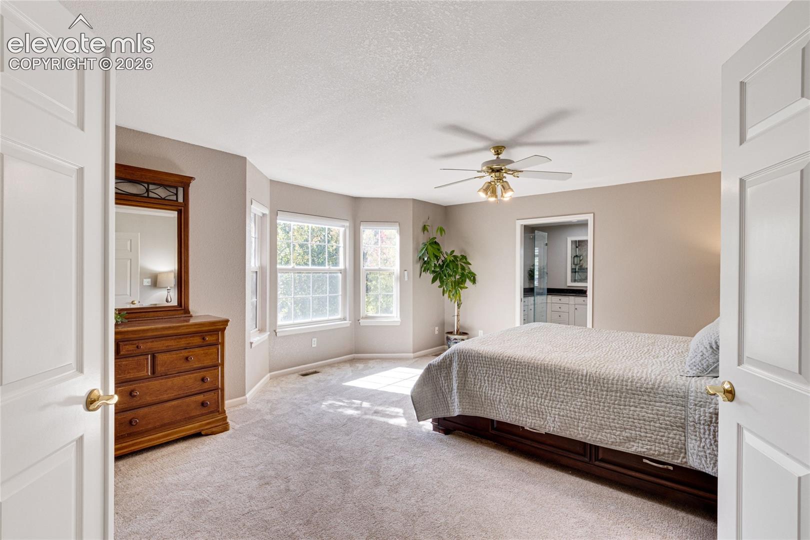 Room featuring double entry doors, a bay window configuration, neutral carpeting, and a ceiling-mounted light fixture with integrated fan