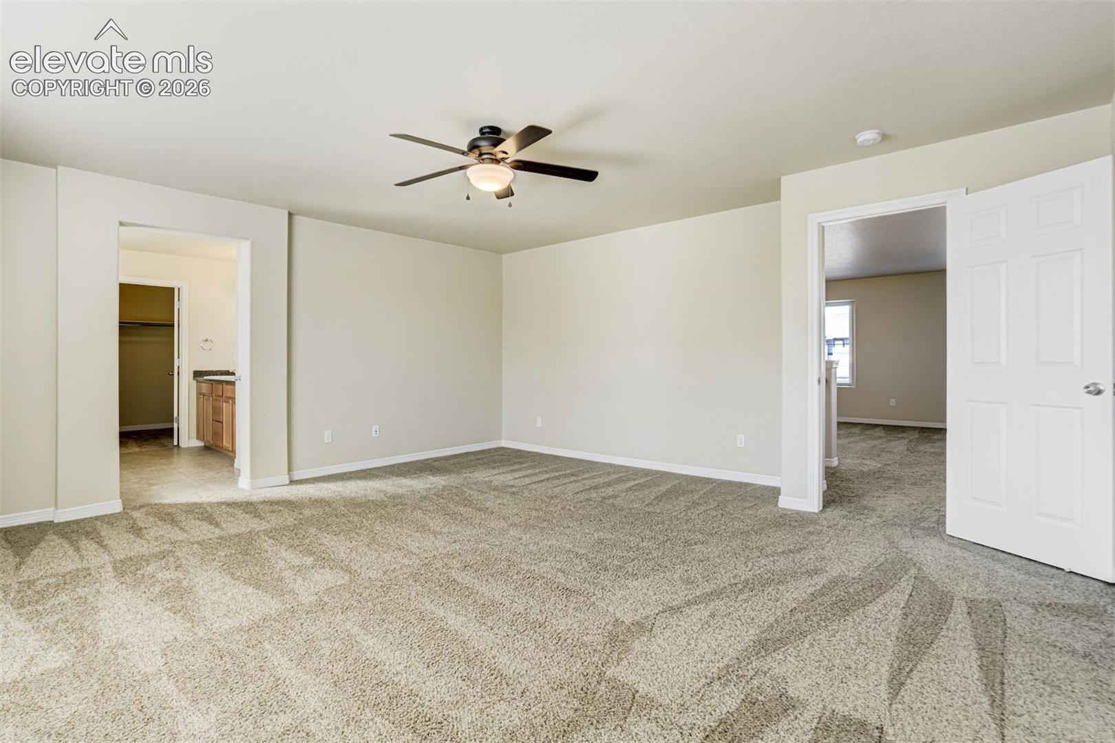 Expansive room featuring neutral-toned walls, patterned carpeting, and a ceiling fan with integrated lighting