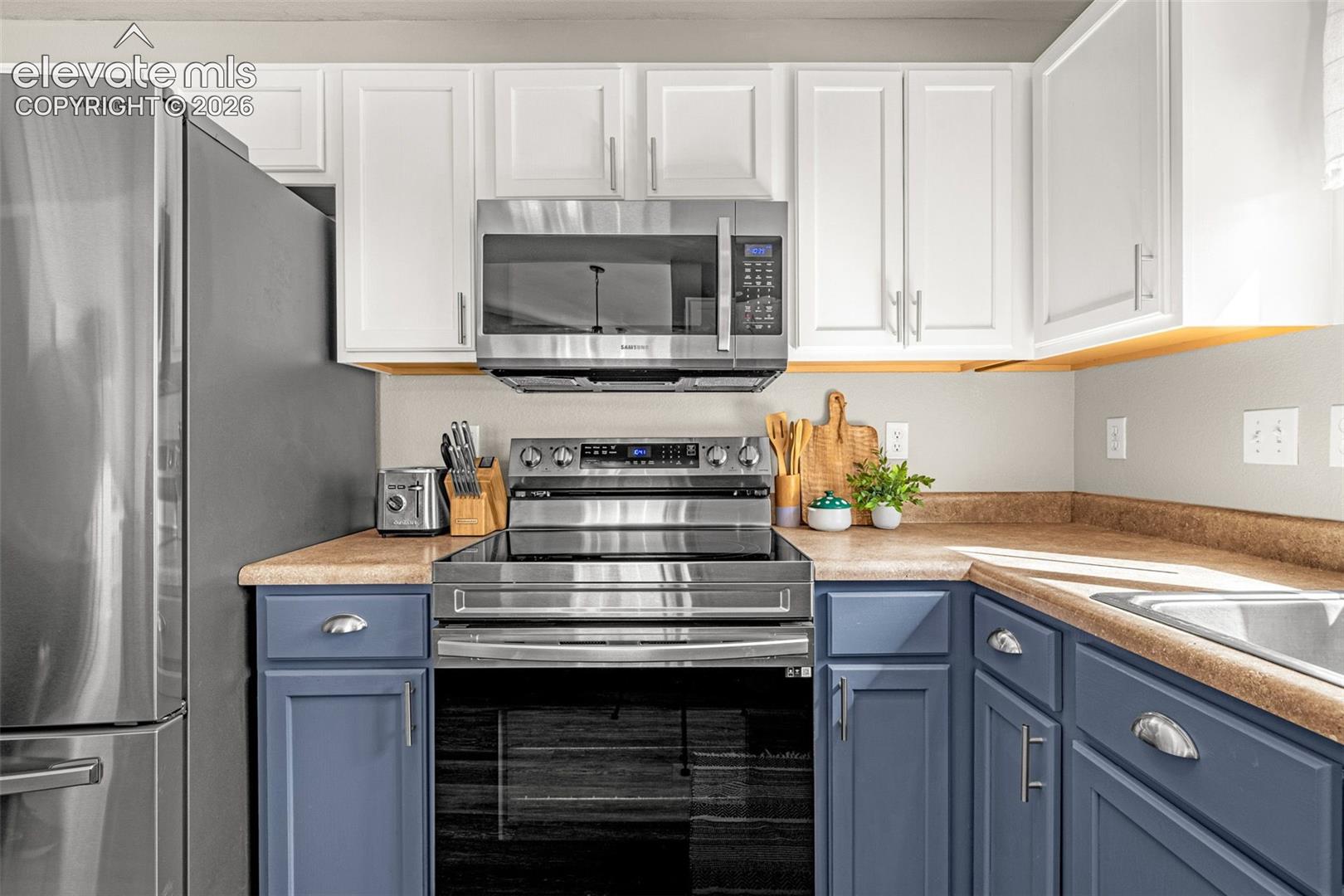White upper cabinetry, blue lower cabinetry, stainless steel appliances, built-in microwave, and a stainless steel sink
