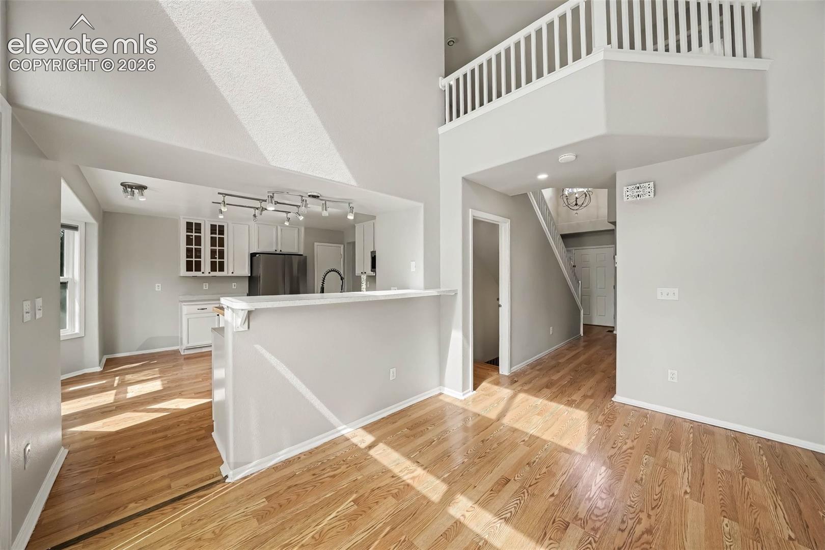 Vaulted ceiling, wood-finish flooring, white kitchen cabinetry, stainless steel appliances, and an upper-level balcony with white railings