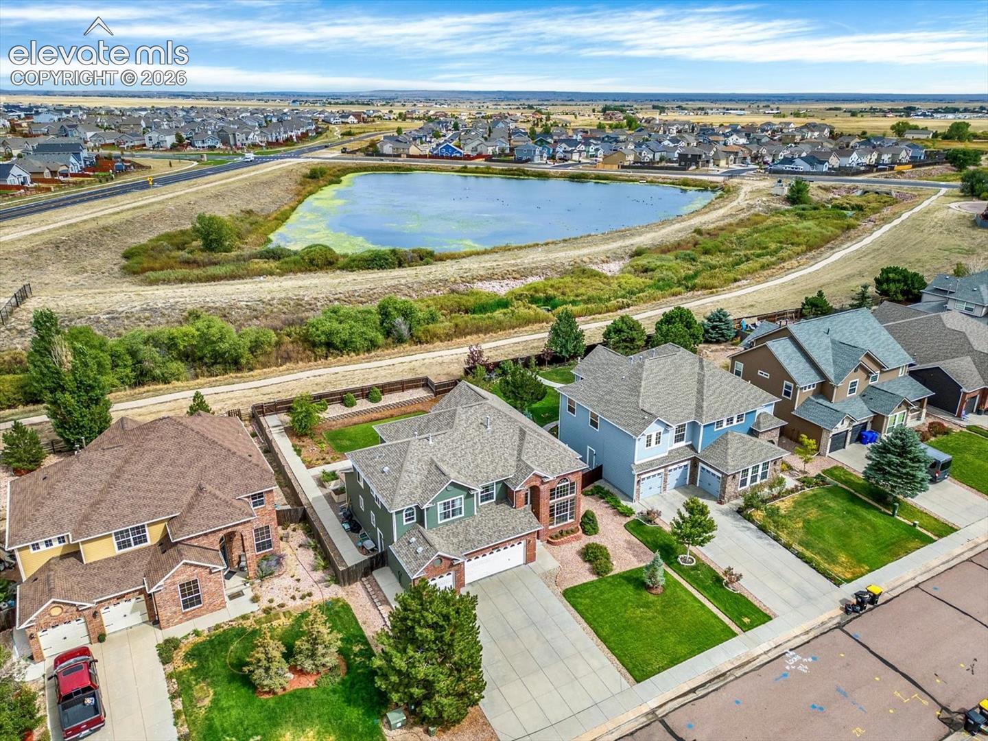 Aerial perspective of a multi-level residential property featuring a multi-gabled roofline, brick and siding exterior, attached multi-car garage, and a manicured lawn