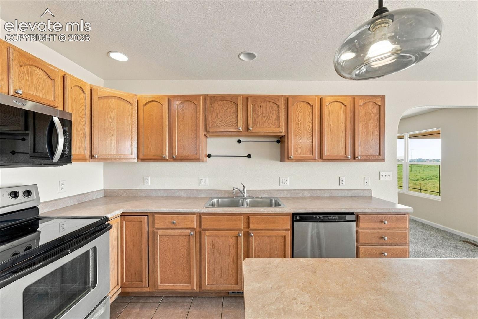 Kitchen featuring light-finish cabinetry, neutral solid-surface countertops, stainless steel appliances, dual-basin sink with pull-down faucet, and recessed and pendant lighting