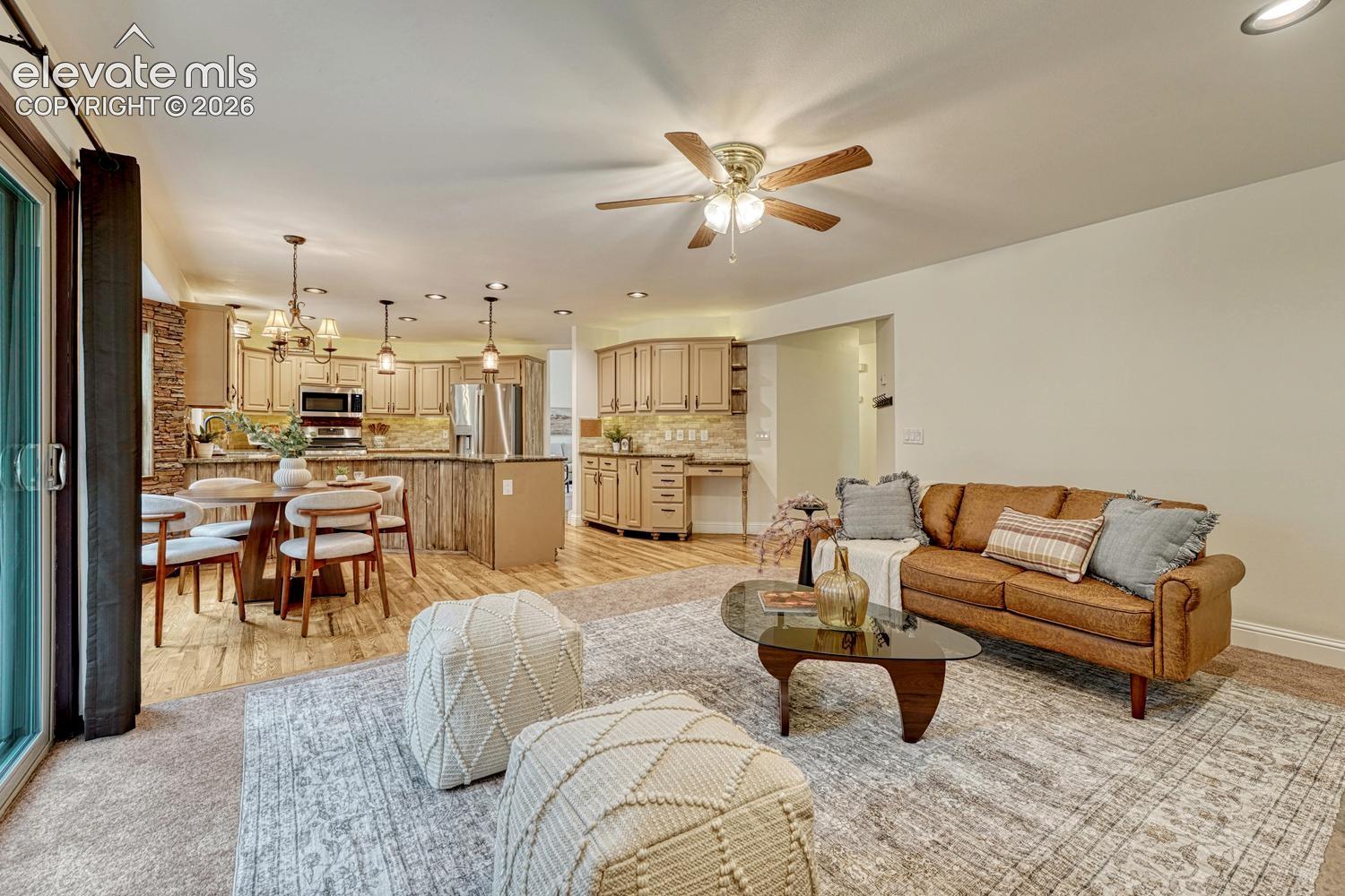 Open-concept living space featuring wood-finish flooring, recessed lighting, a ceiling fan, cabinetry with integrated desk space, and a sliding glass door