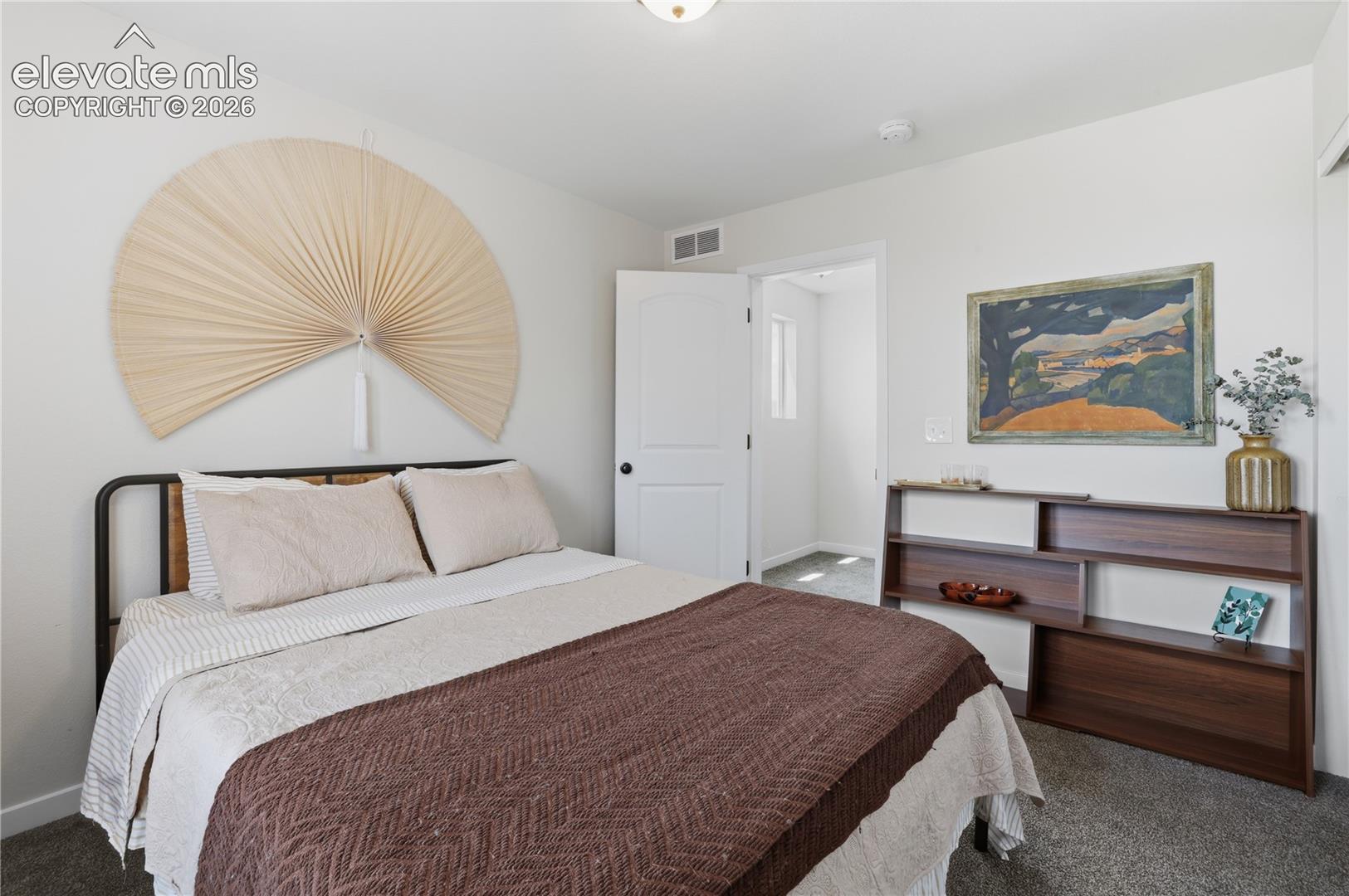 Bedroom featuring light gray walls, dark gray carpet, a white paneled door, and a built-in wood-finish shelving unit