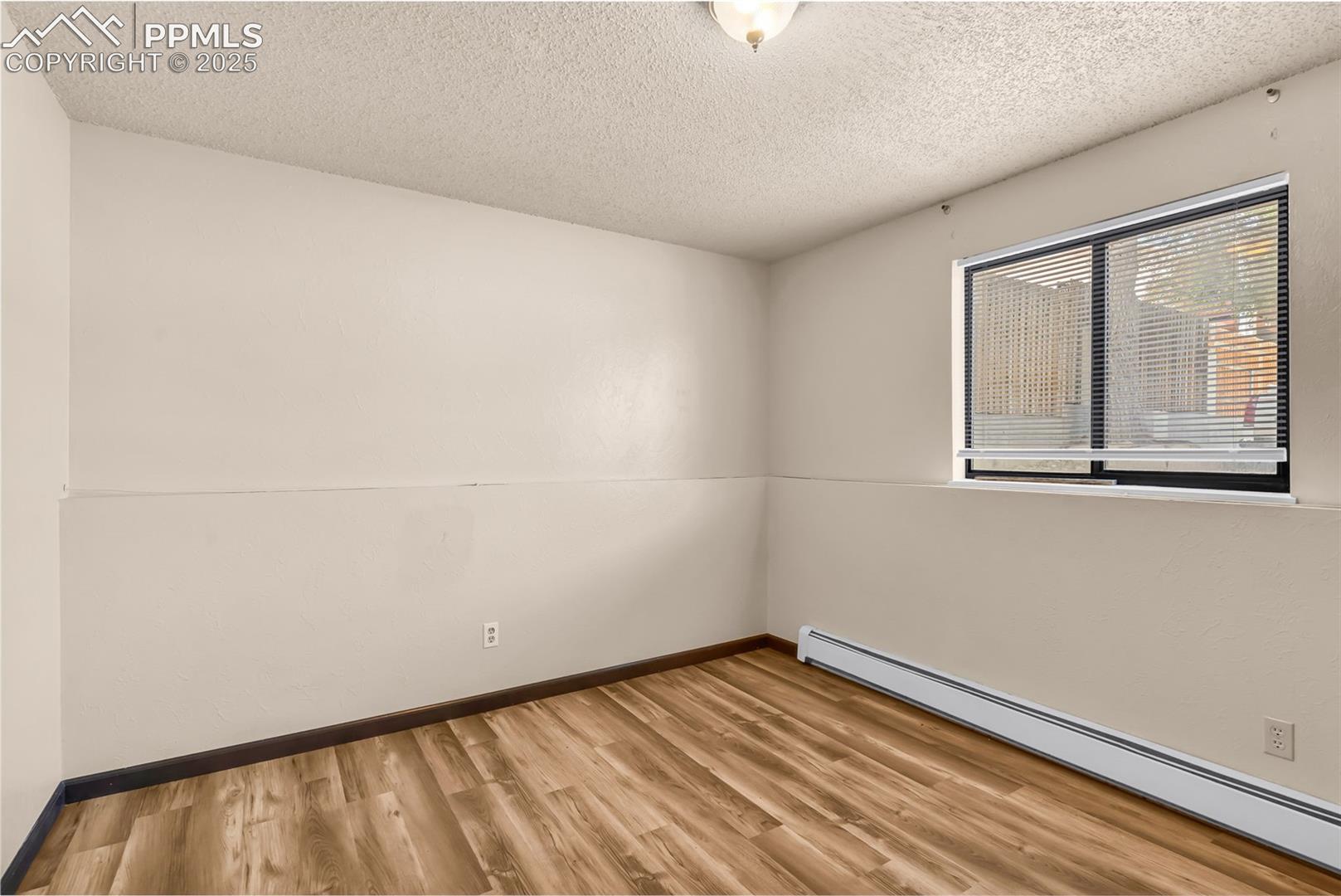 Empty room featuring baseboard heating, light wood finished floors, and a textured ceiling