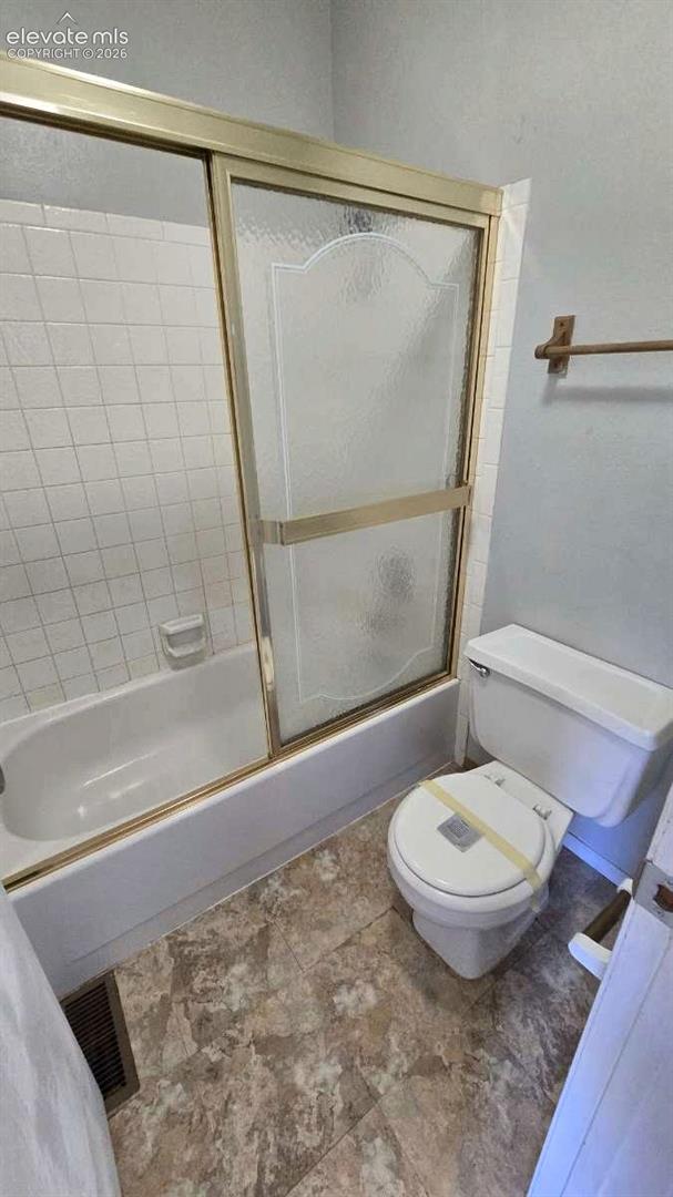 Bathtub with a sliding glass door enclosure, white wall tile surround, floor-mounted toilet, and patterned tile flooring
