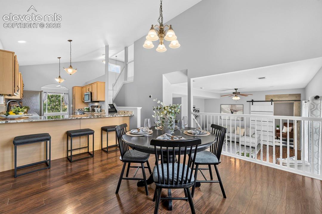 Open-concept interior featuring vaulted ceilings, wood-finish flooring, a kitchen breakfast bar with stone-surfaced countertops, and a white balustrade railing