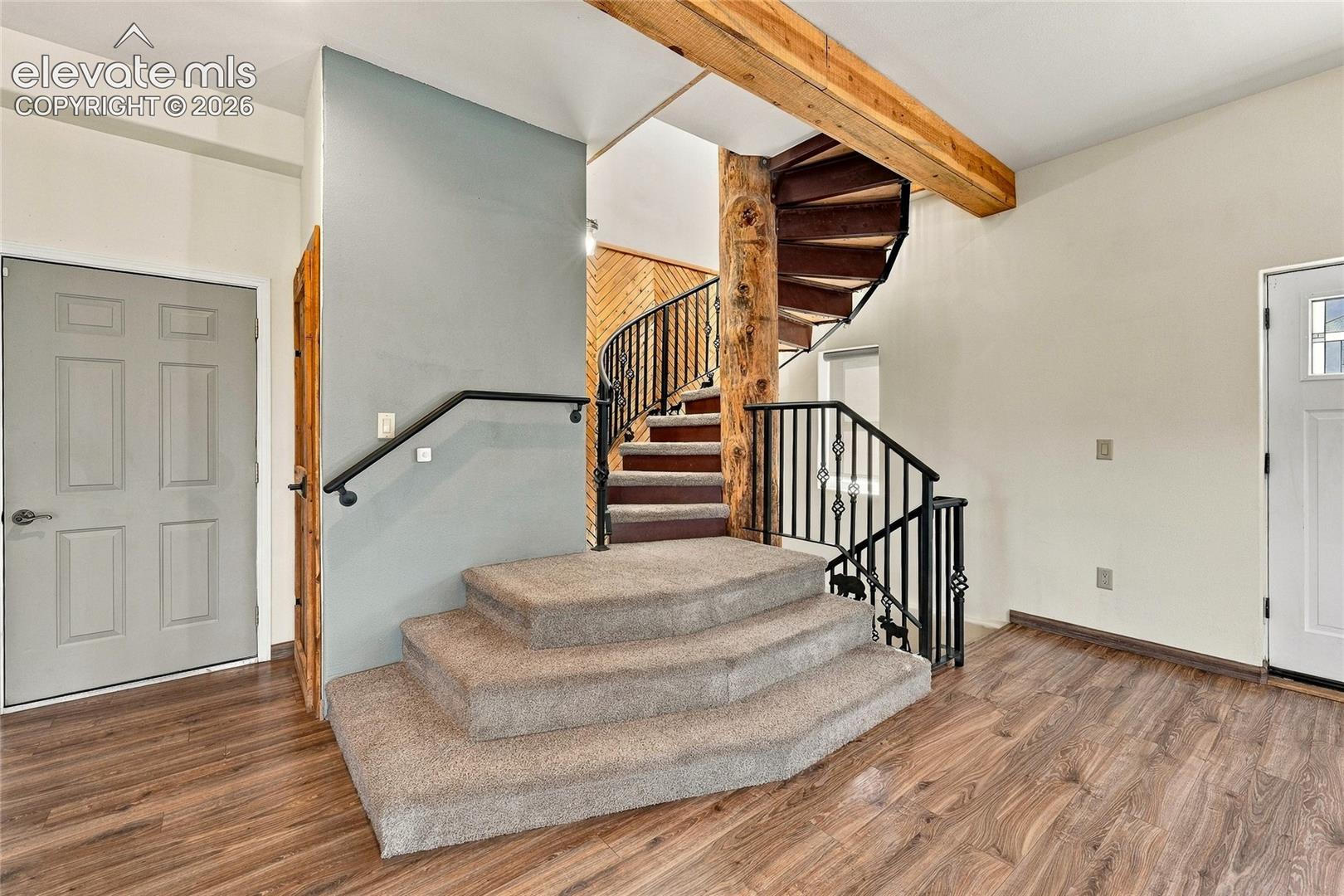 Spiral staircase featuring a structural log support, custom iron railings, wood-finish flooring, and multi-level carpeted steps