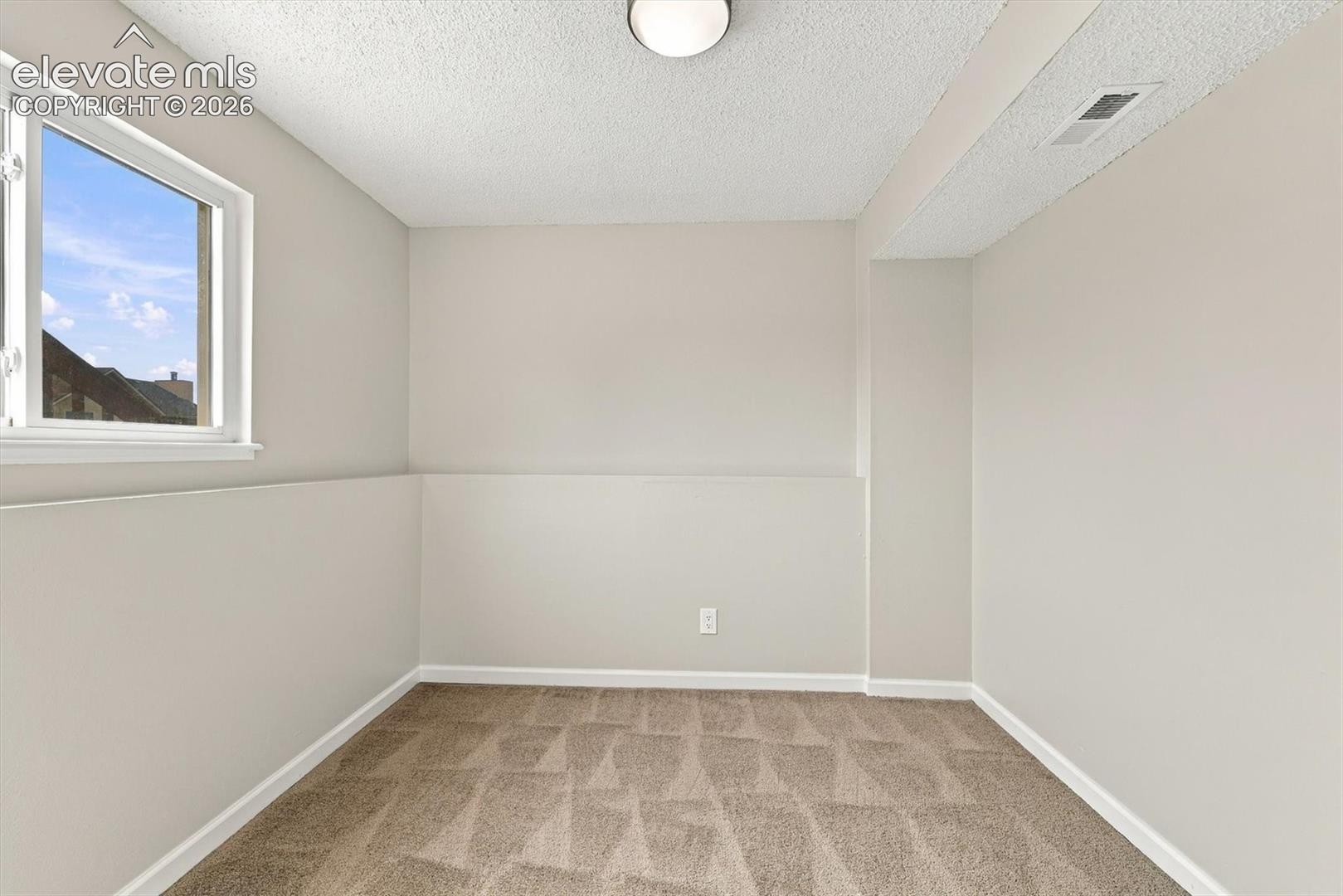 Neutral-toned interior space featuring wall-to-wall carpeting, a single window, and a ceiling-mounted light fixture
