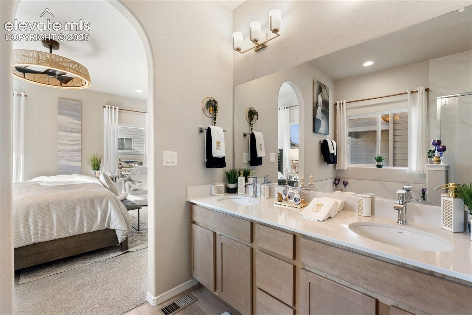 Dual-sink vanity with light wood-finish cabinetry, solid-surface countertop, full-width mirror, and three-light wall fixture