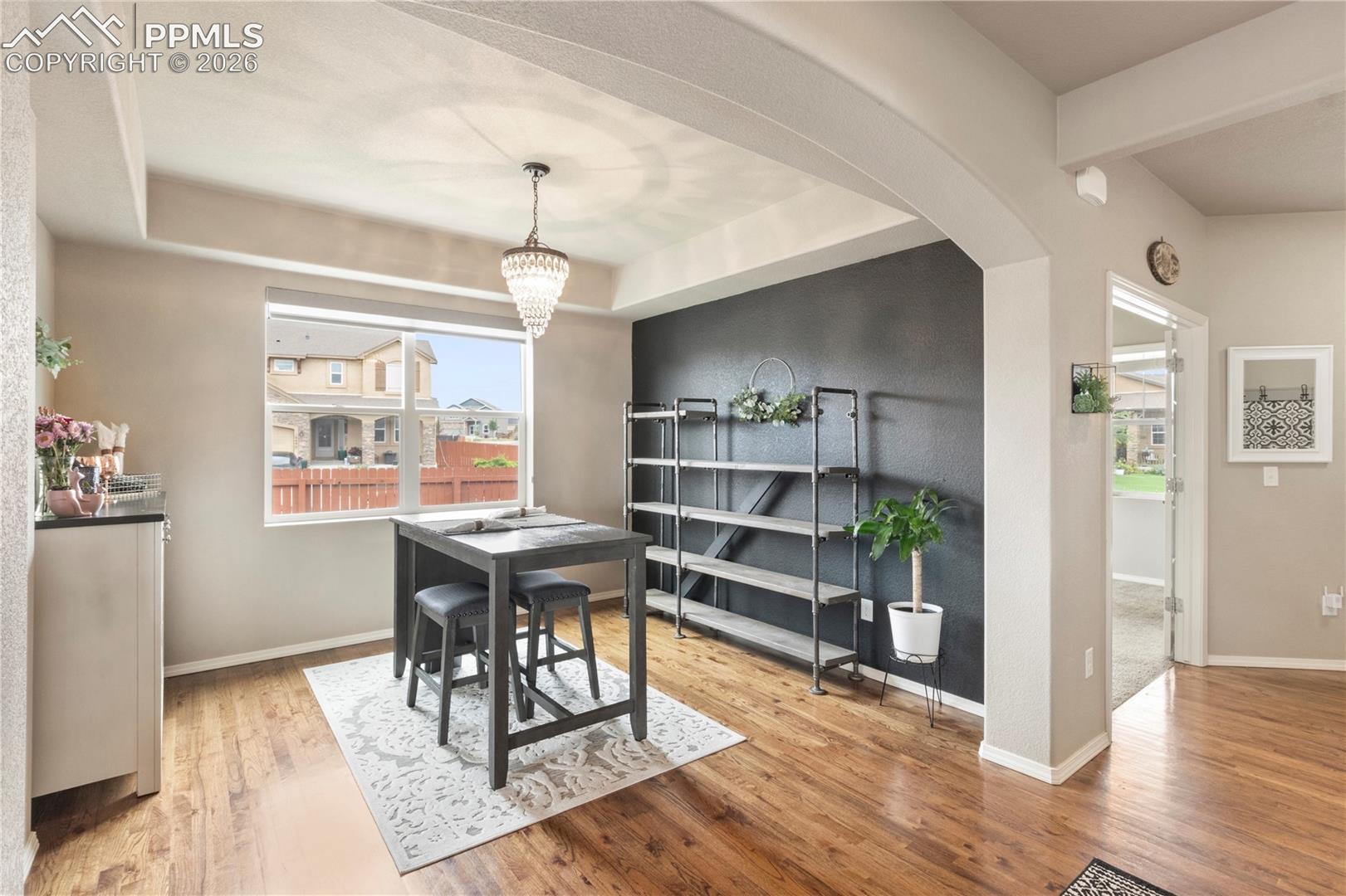 Dining area with light wood-type flooring, a tray ceiling, a chandelier, arched walkways, and beamed ceiling
