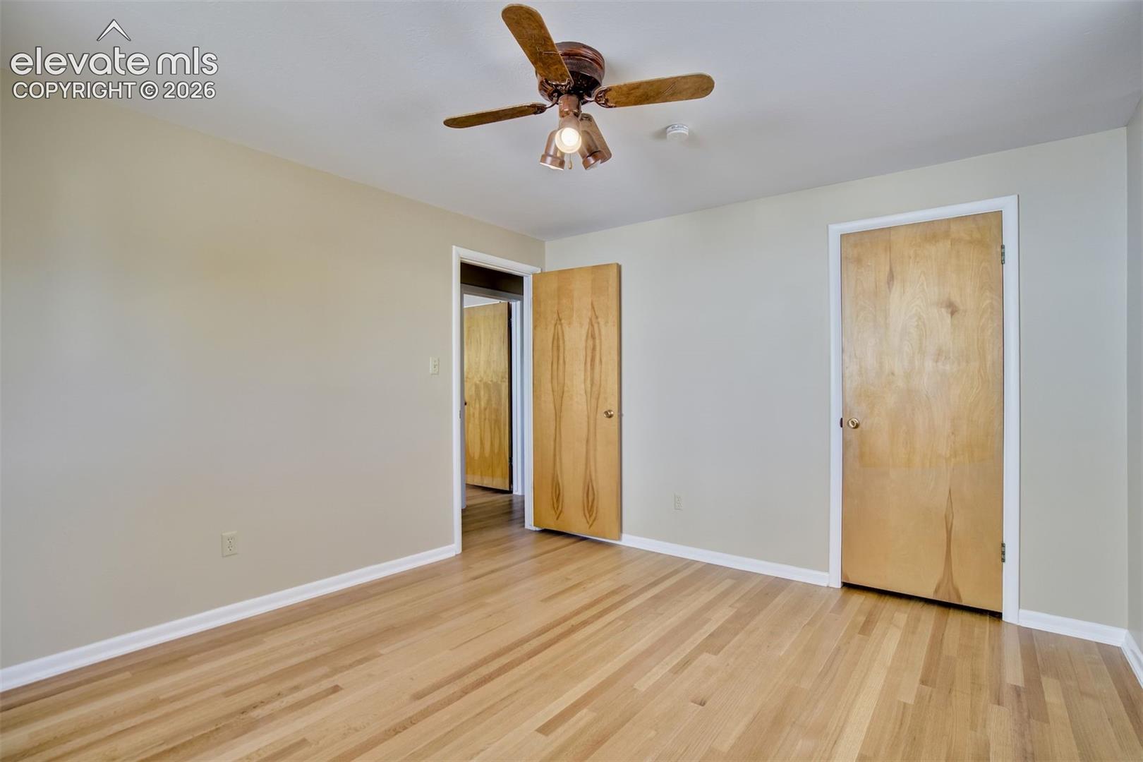 Interior space featuring wood-finish flooring, neutral wall tones, flat-panel wood doors, and a ceiling-mounted fan with integrated lighting