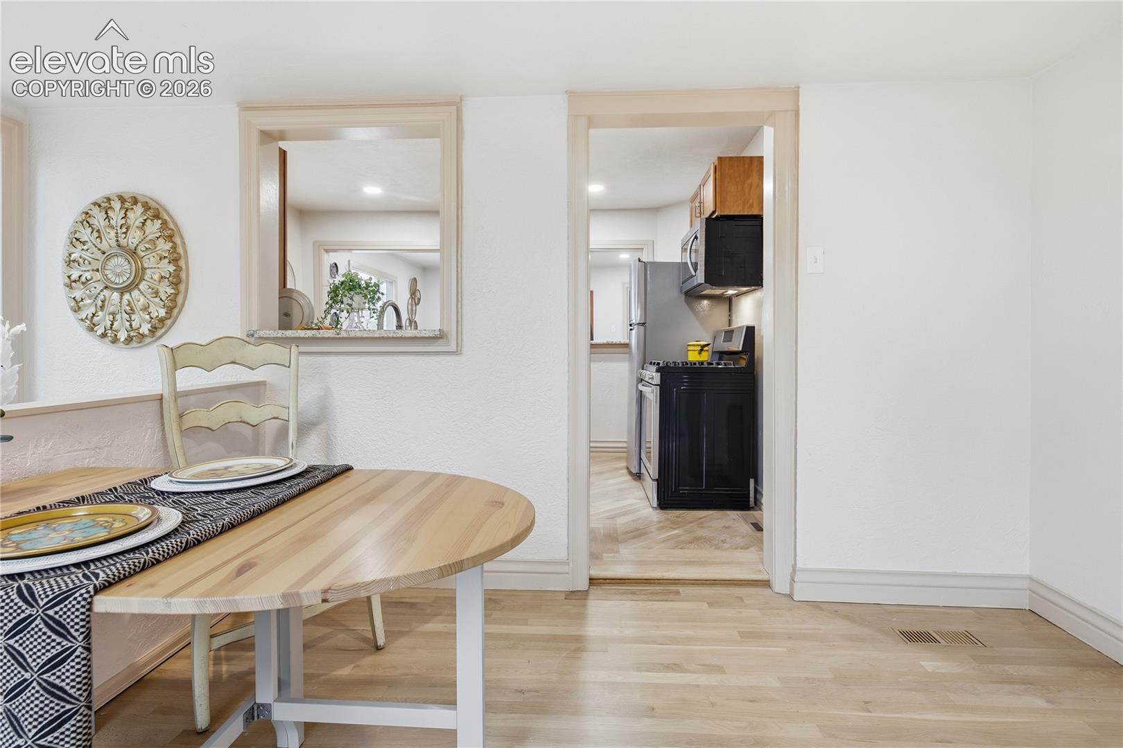 Light-toned wood-finish flooring, built-in pass-through wall window, and structured doorway entry leading to kitchen with black range and built-in upper cabinetry