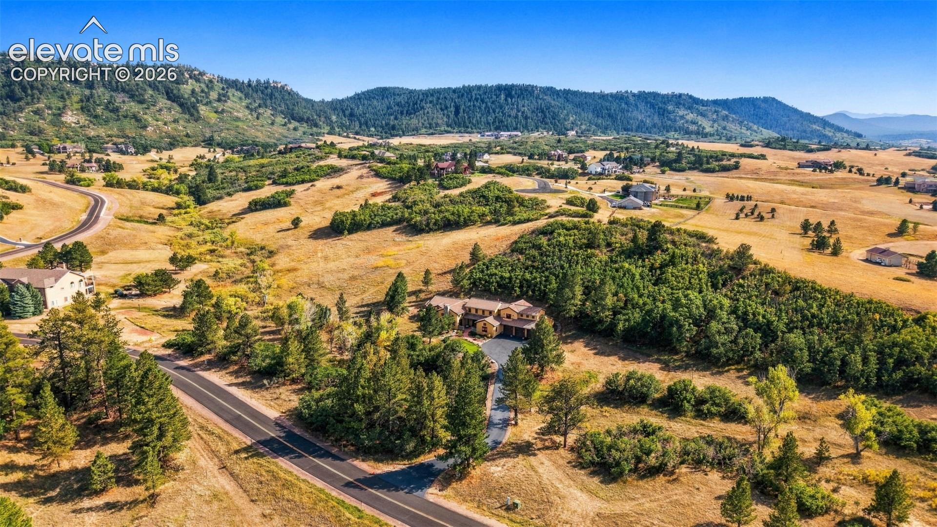 Expansive property with a stucco exterior, a paved driveway, and mature landscaping, set against a backdrop of rolling hills and distant mountains