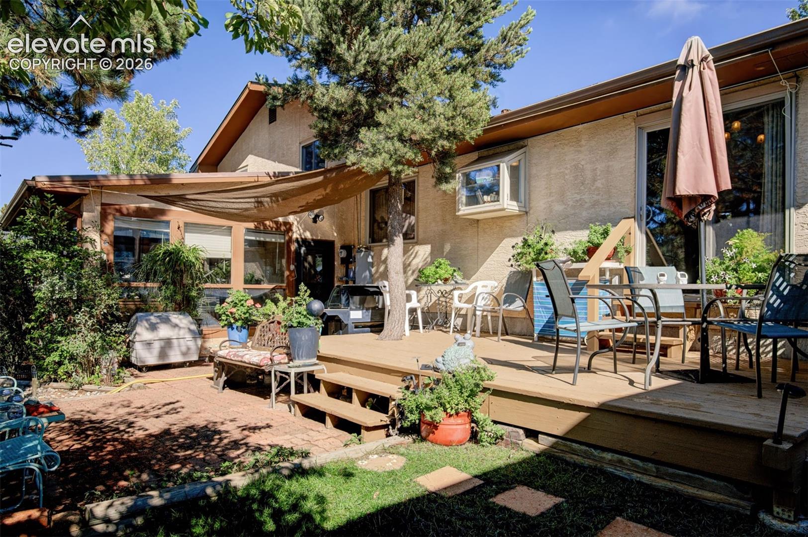 Expansive outdoor living area featuring a multi-level wood deck, a brick patio, mature trees, and a shade sail