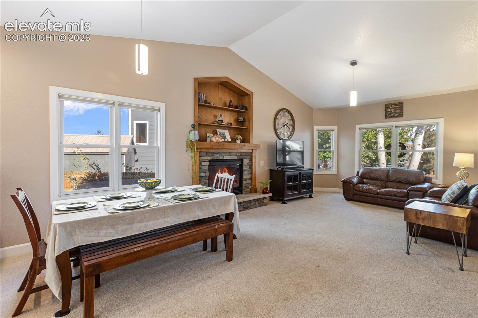Vaulted ceilings, stone-faced fireplace with wood mantel, built-in shelving, and large windows