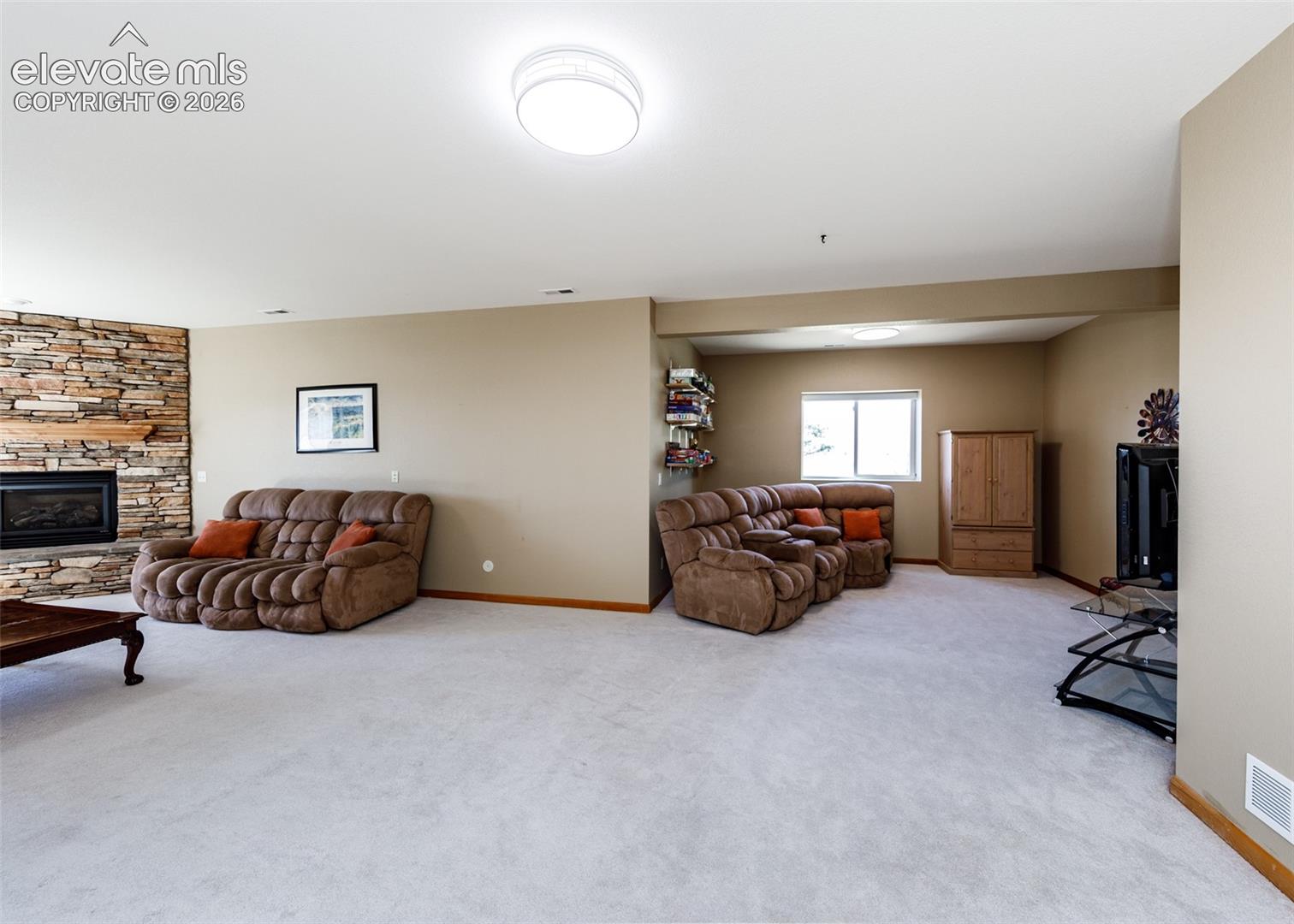 Spacious interior with neutral carpeting, stone-clad fireplace, and integrated lighting