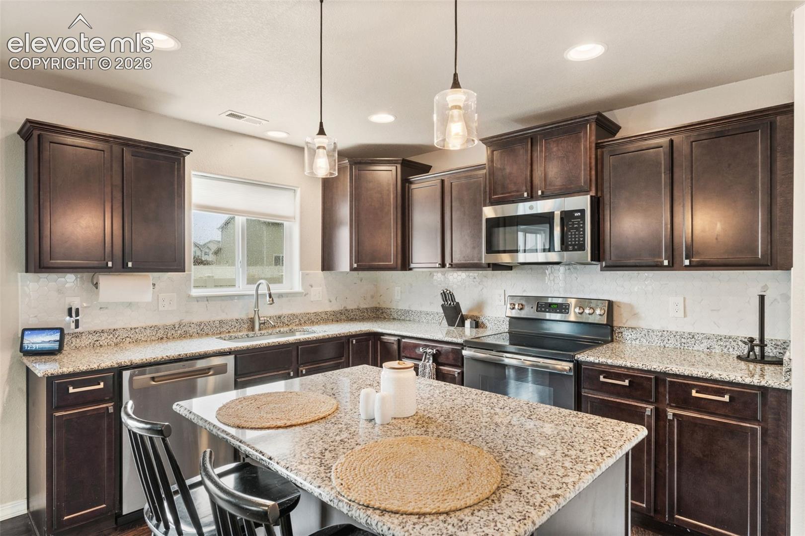 Kitchen featuring dark wood cabinetry, light-toned countertops, stainless steel appliances, and recessed lighting