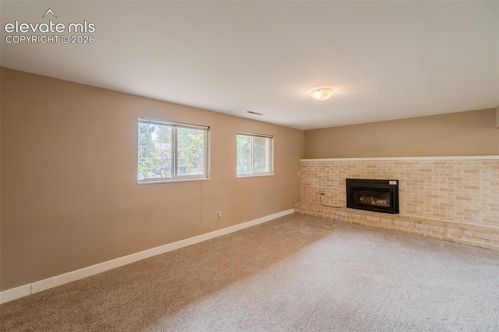 Recessed fireplace with a light brick surround, neutral wall paint, two windows, and a flush mount light fixture