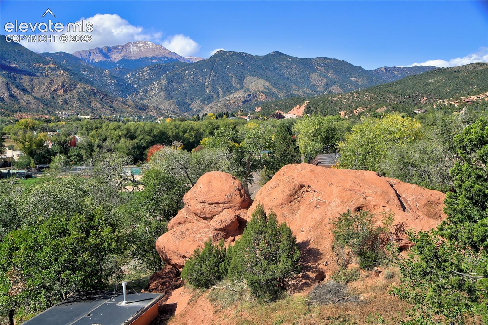 Prominent red rock formations, mature deciduous and evergreen trees, and a mountain range backdrop