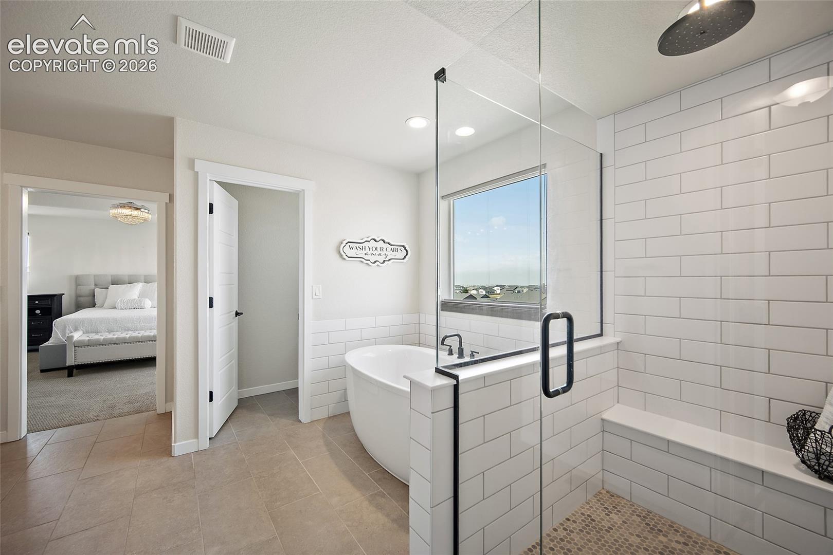 Freestanding soaking tub, glass-enclosed shower with subway tile surround, rain shower head, built-in shower bench, and large window