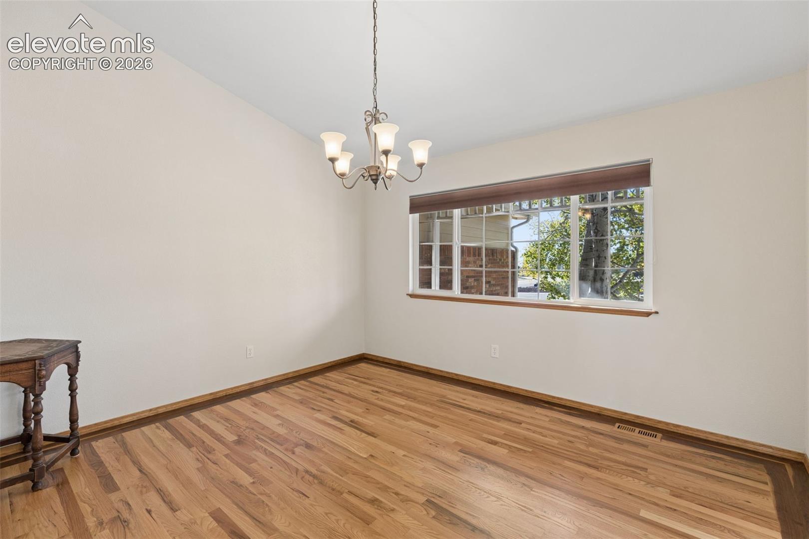 Wood-finish flooring, vaulted ceiling, multi-pane window with wood-trim finish, and a central five-light chandelier