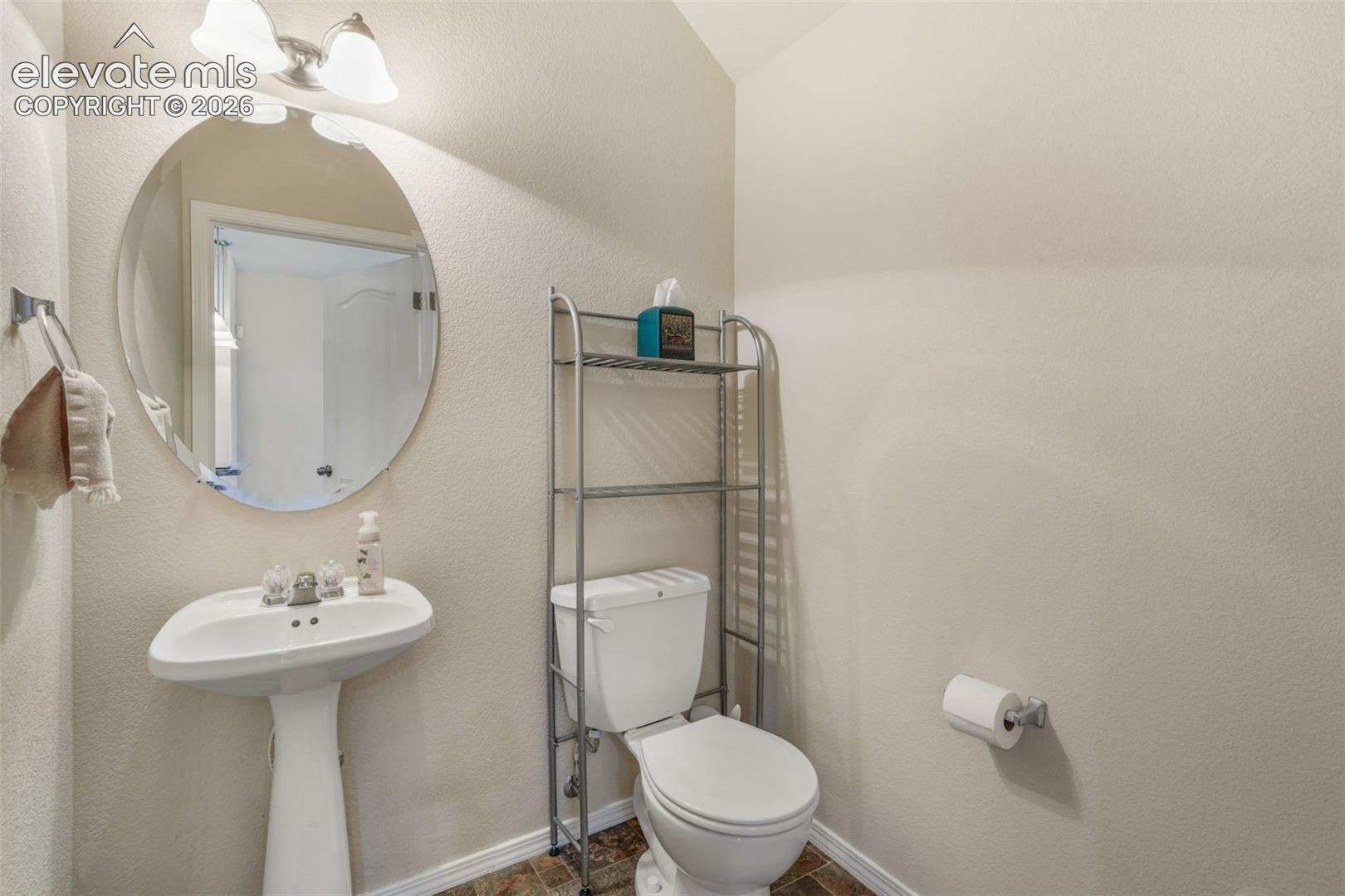 Pedestal sink with chrome faucet, oval mirror, wall-mounted light fixture, and tile flooring