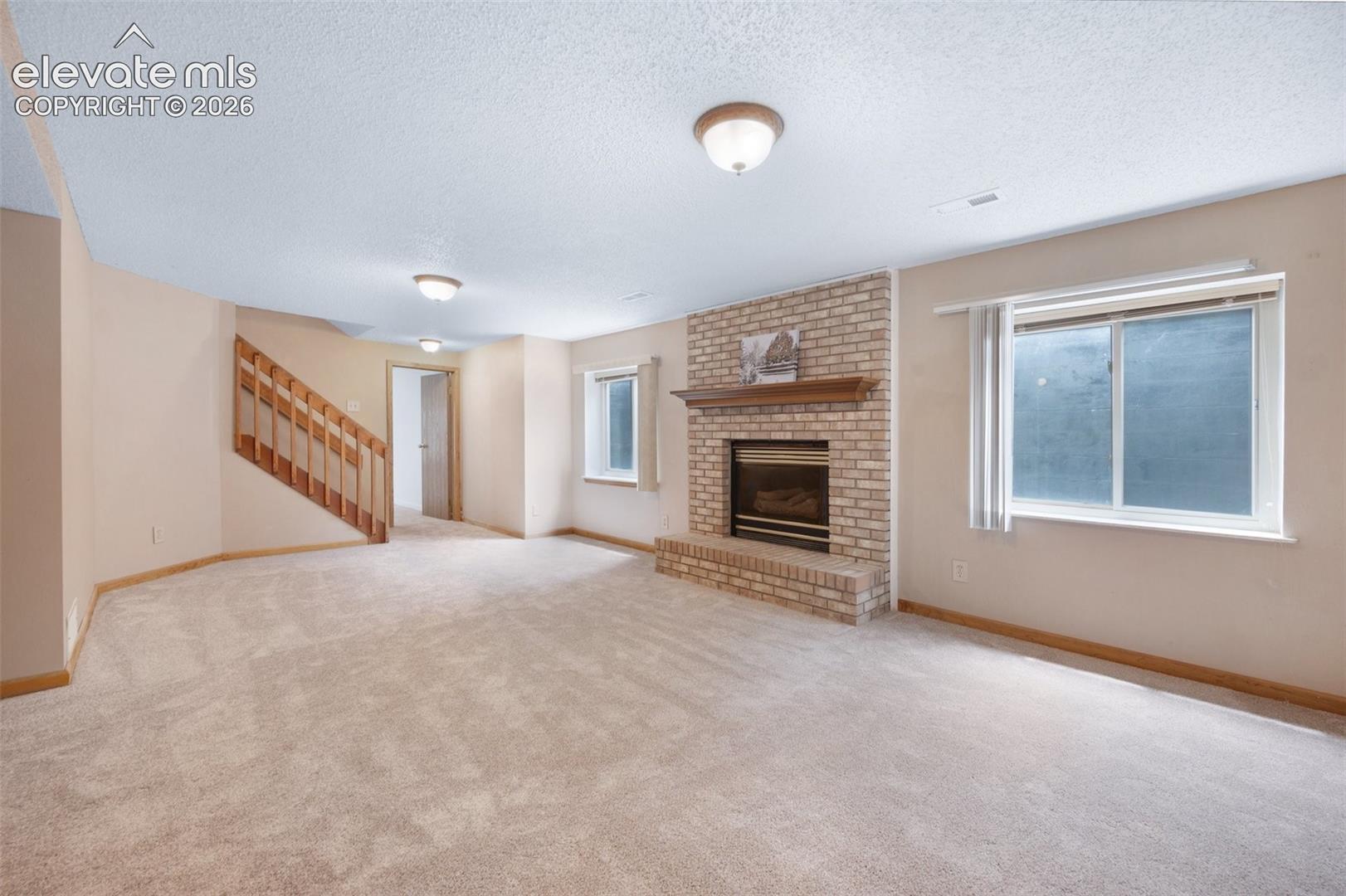 Unfurnished living room with stairway, a textured ceiling, plenty of natural light, baseboards, and a brick fireplace