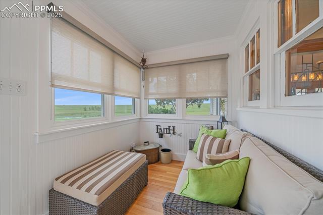 Sunroom featuring healthy amount of natural light, wood finished floors, wooden walls, and ornamental molding