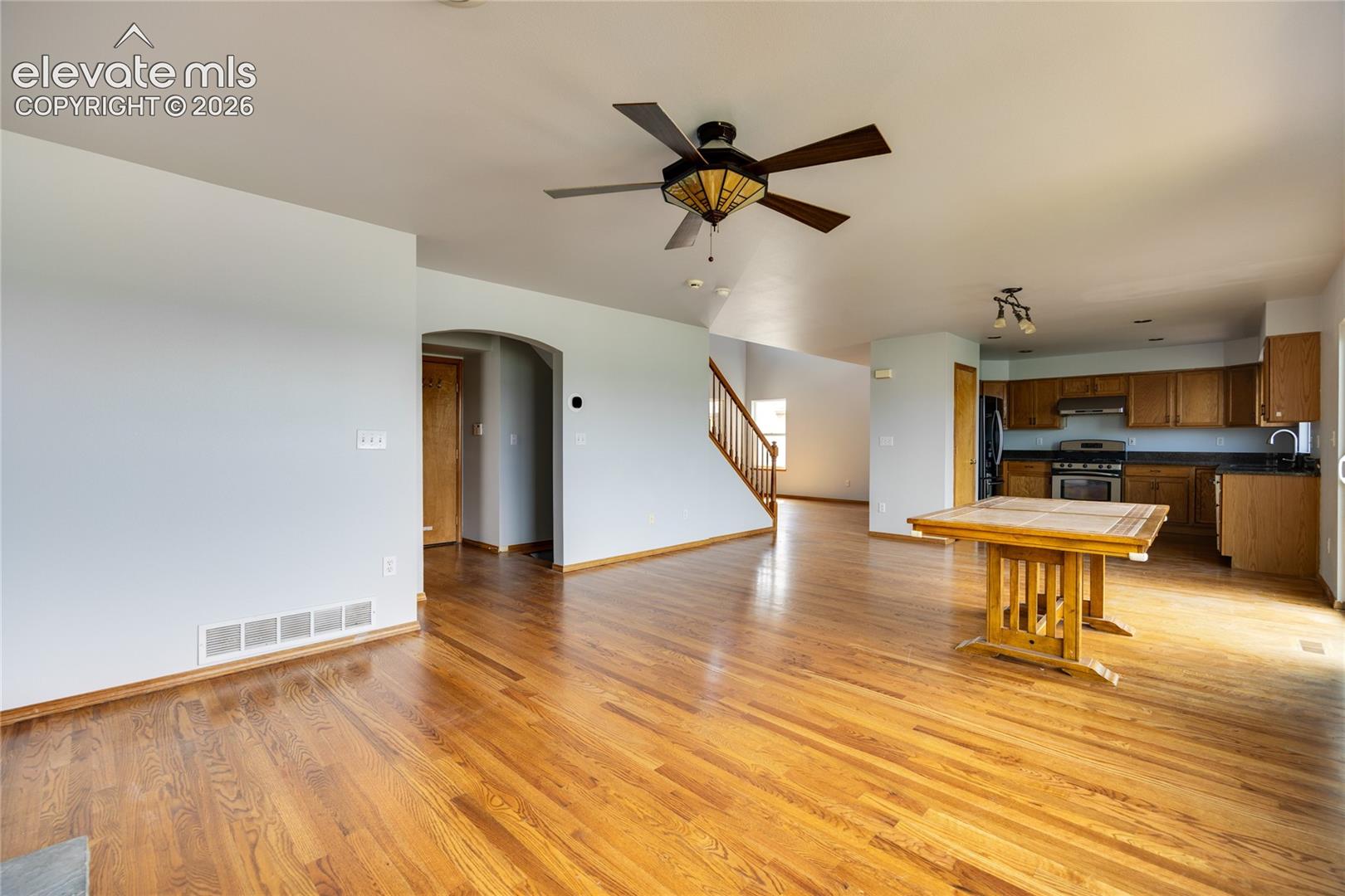 Open-concept living space with wood-finish flooring, a ceiling fan with integrated lighting, and an arched entryway