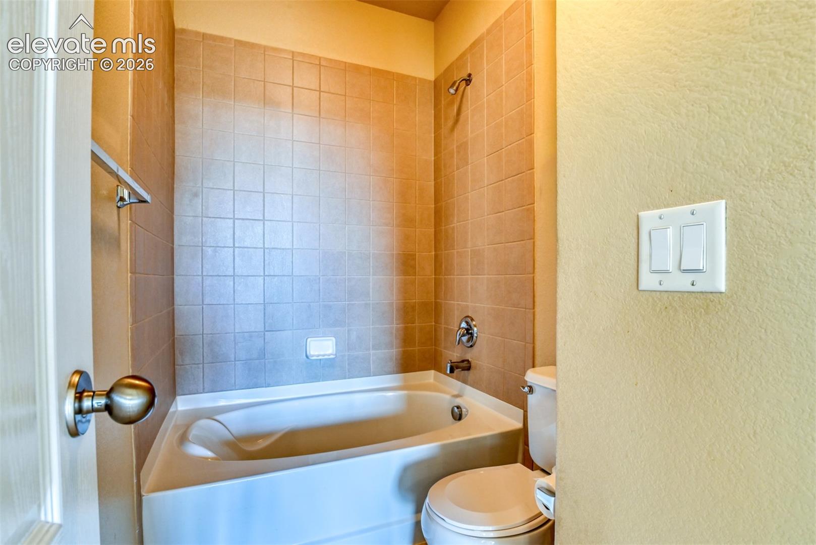 Full-size bathtub with surrounding square tile backsplash, wall-mounted shower head, chrome fixtures, and built-in soap dish