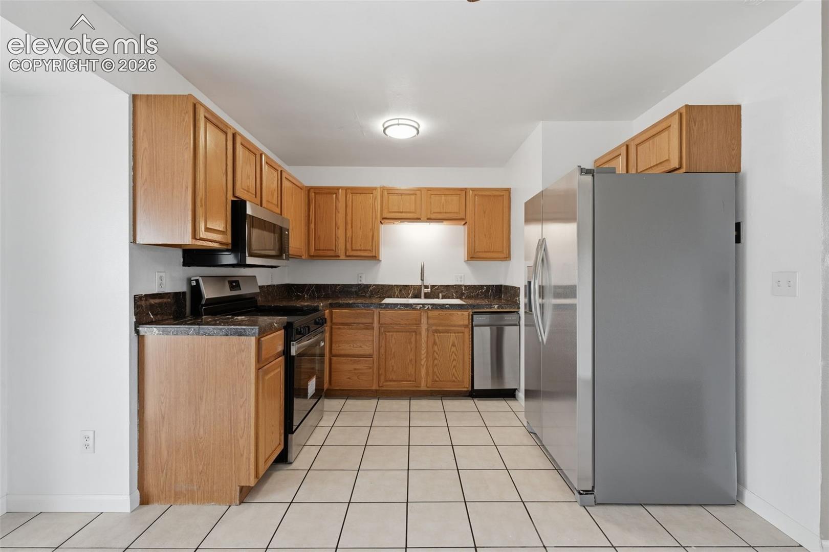 U-shaped kitchen with wood-finish cabinetry, dark countertops, and stainless steel appliances