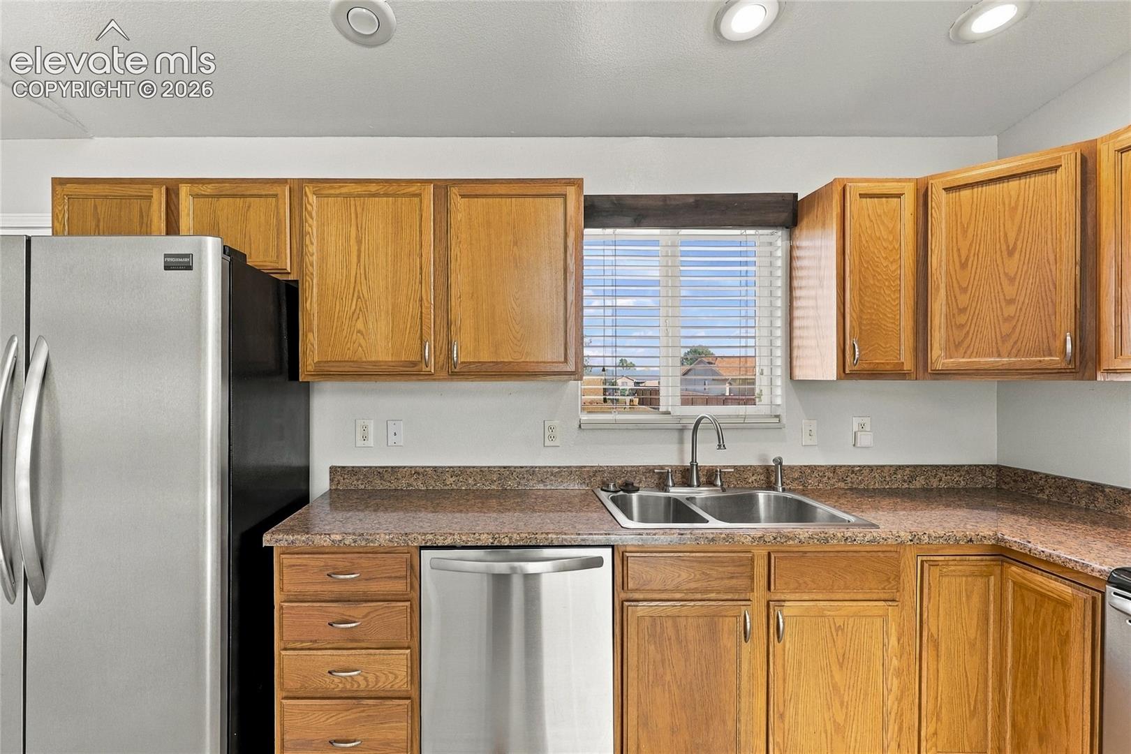 Kitchen featuring wood cabinetry, stone-finish countertops, stainless steel dual-basin sink with a gooseneck faucet, and recessed ceiling lighting