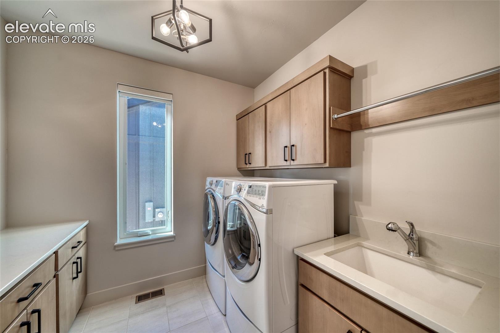 Laundry area featuring wood-finish cabinetry, solid-surface countertops, a deep basin sink with a metal faucet, tile flooring, and geometric-style overhead lighting