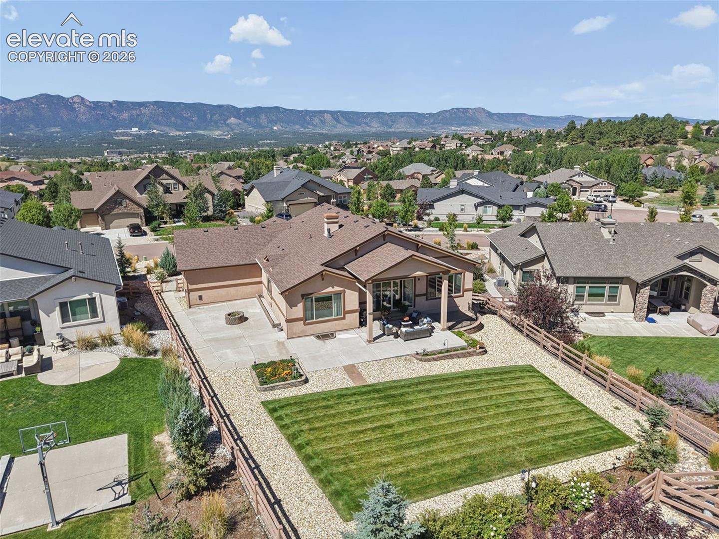 Rear exterior featuring a covered patio, extensive concrete hardscaping, large lawn area, and gravel landscaping
