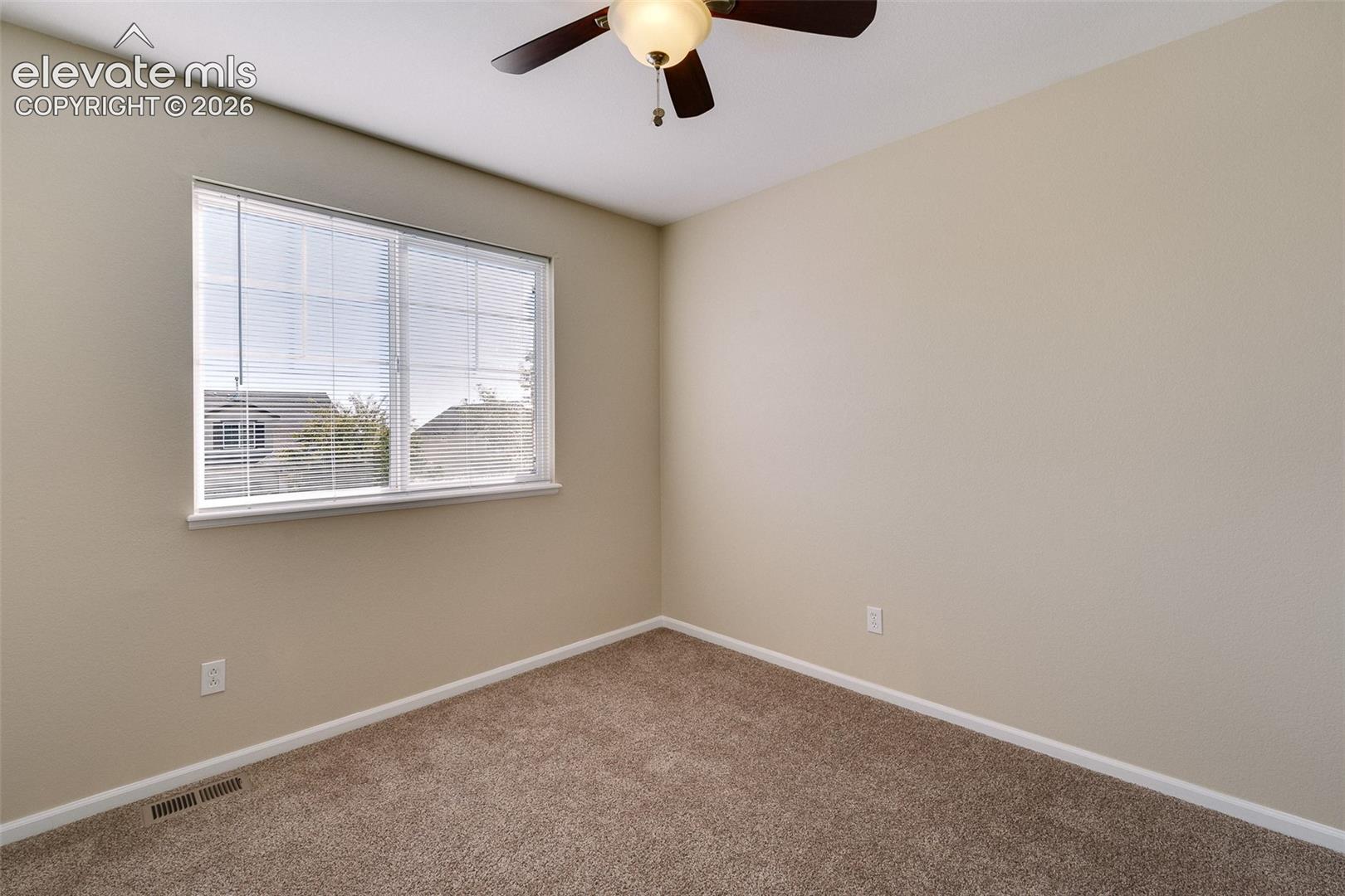 Neutral-toned interior space featuring wall-to-wall carpeting, a multi-blade ceiling fan with integrated lighting, and a large window with horizontal blinds