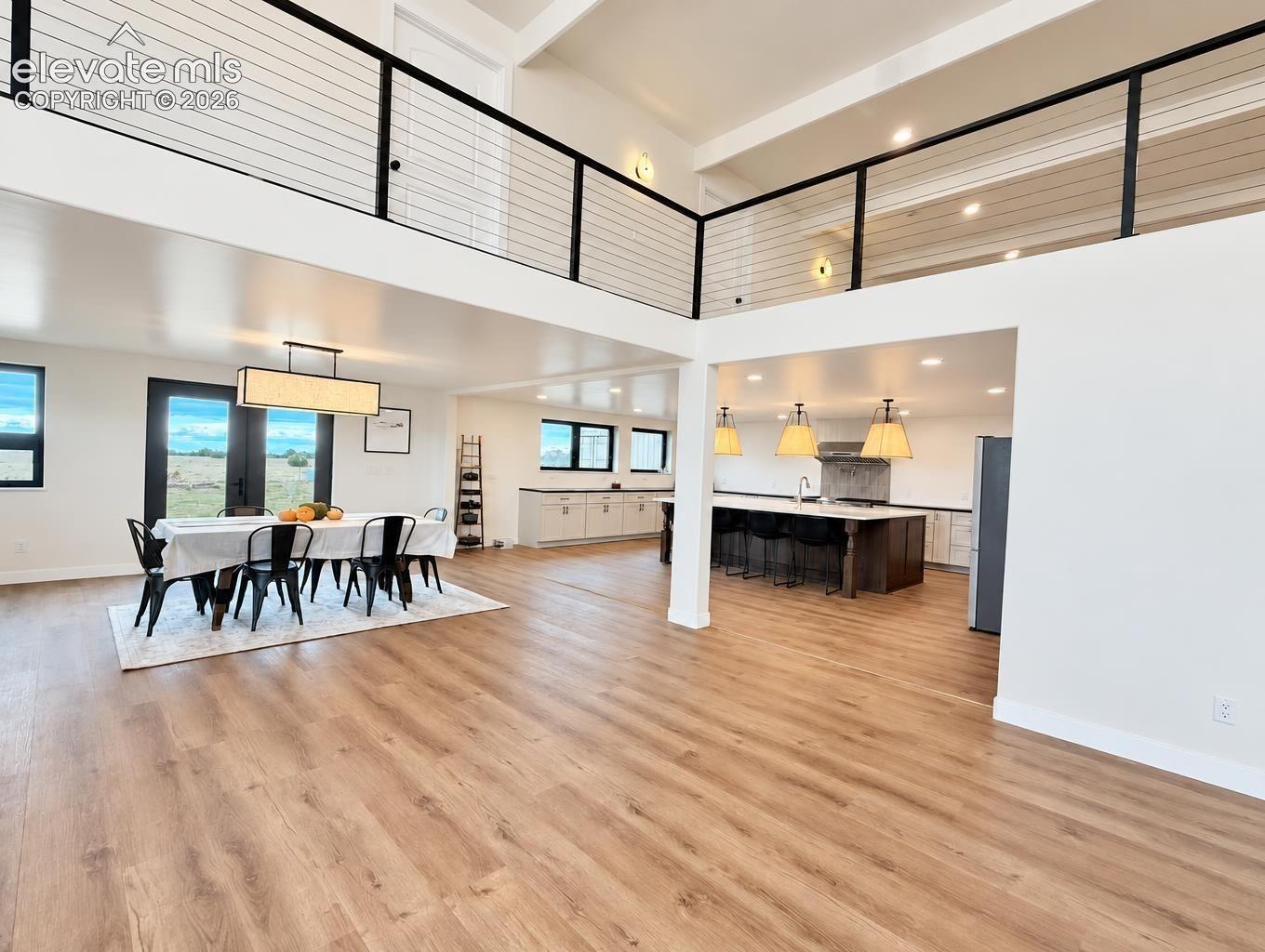 Open-concept interior featuring wood-finish flooring, a kitchen island with stone countertops, vaulted ceilings, and a metal cable railing system