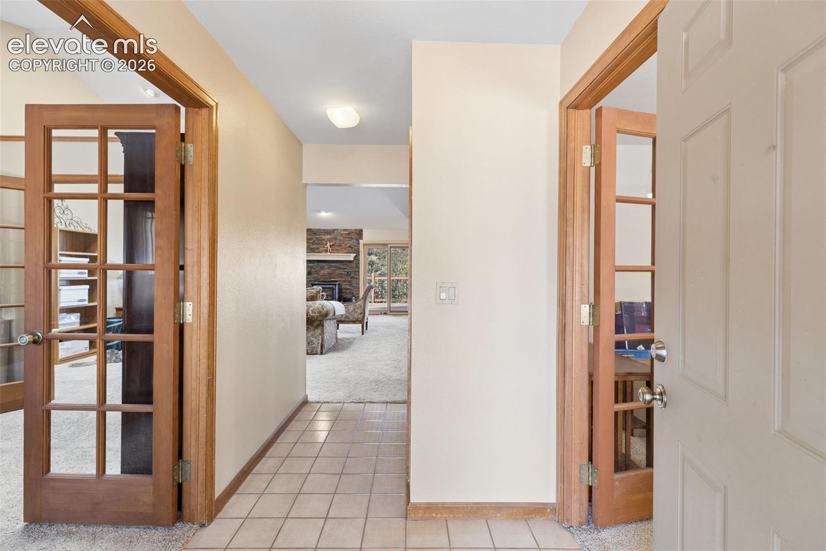 Entryway featuring light-toned tile flooring, natural wood-finish door frames, and dual sets of glass-paneled doors