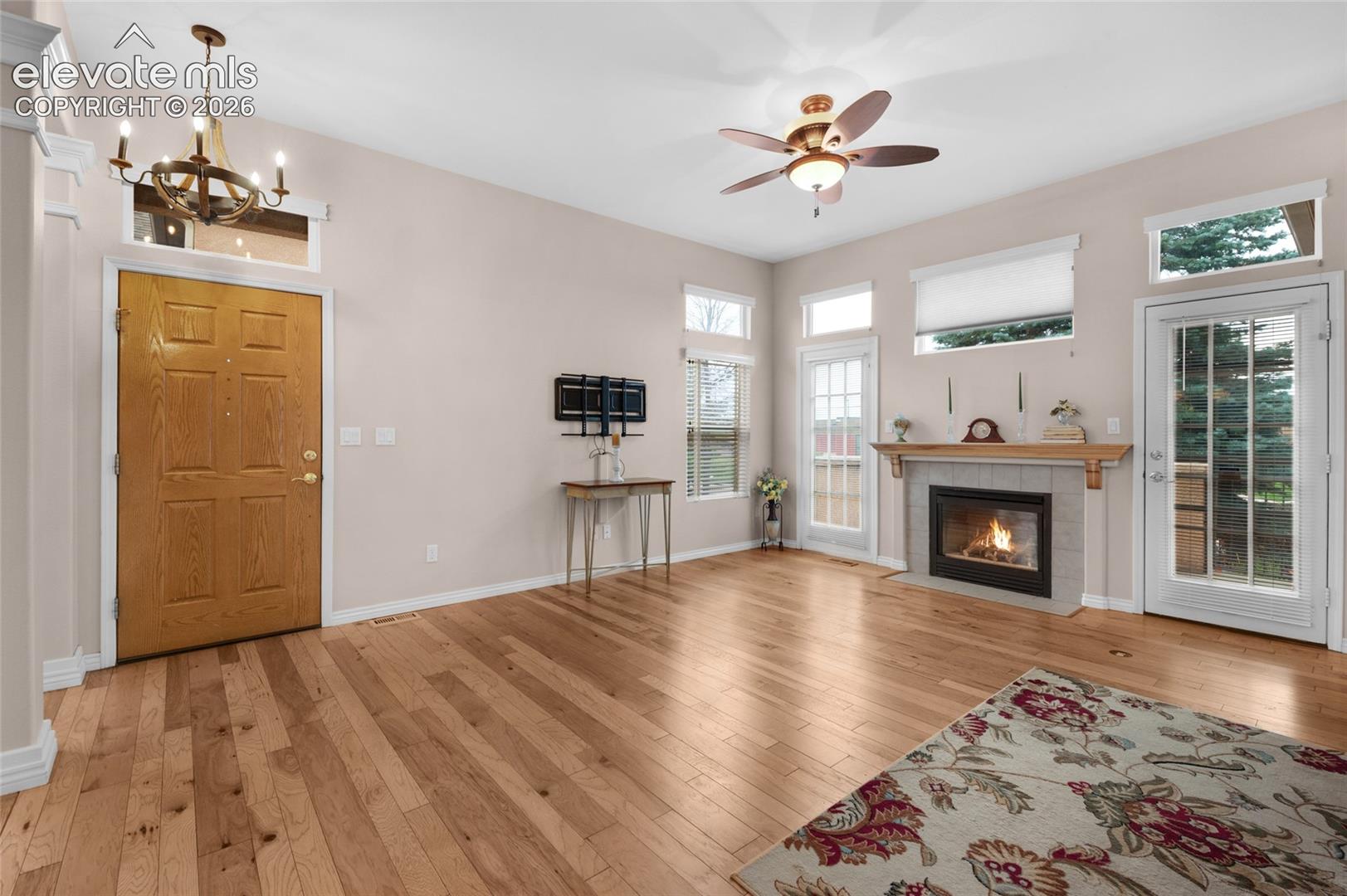 Open-concept living space featuring wood-finish flooring, vaulted ceilings, a fireplace with a stone surround and mantel, and multiple glass-paneled exterior doors