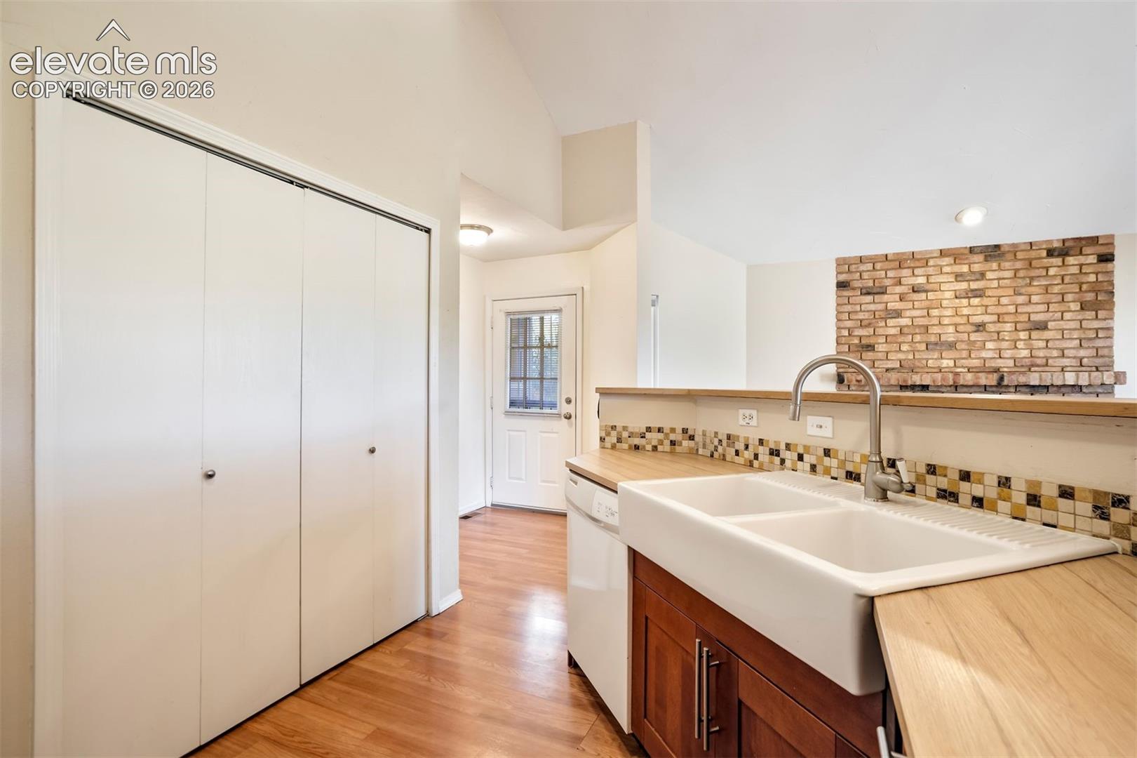 Kitchen featuring a white dual-basin apron-front sink, wood-finish countertop, mosaic tile backsplash, and wood-finish cabinetry