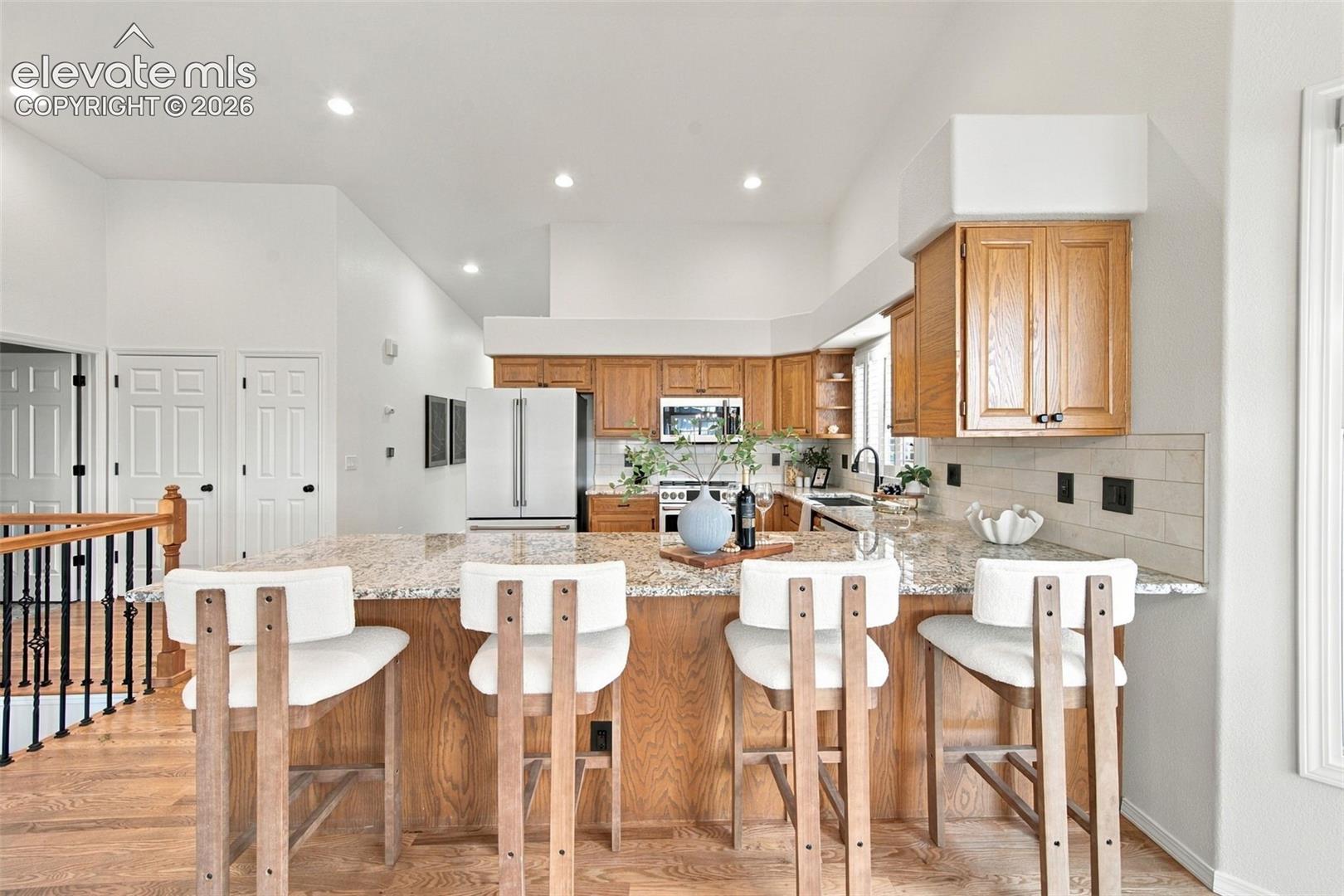 Kitchen featuring natural wood cabinetry, stone-surface breakfast bar, recessed lighting, and tile backsplash