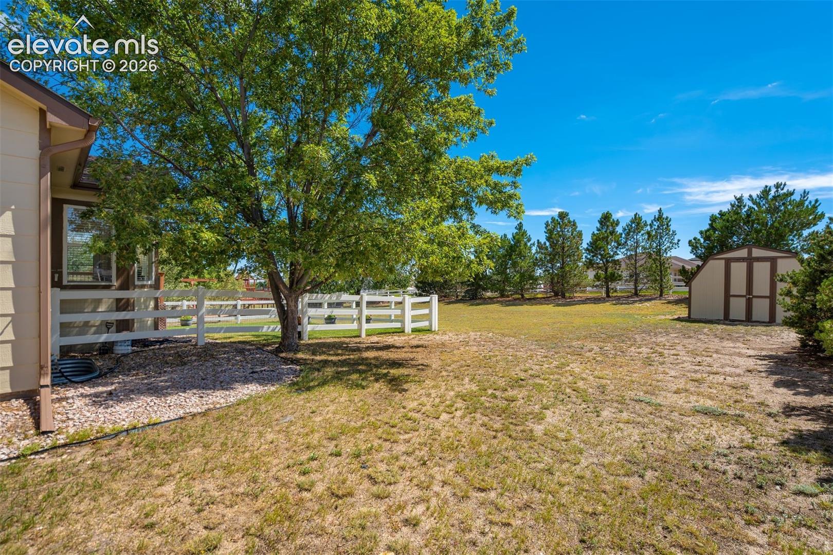 Spacious backyard featuring a detached storage shed, white vinyl perimeter fencing, and mature trees